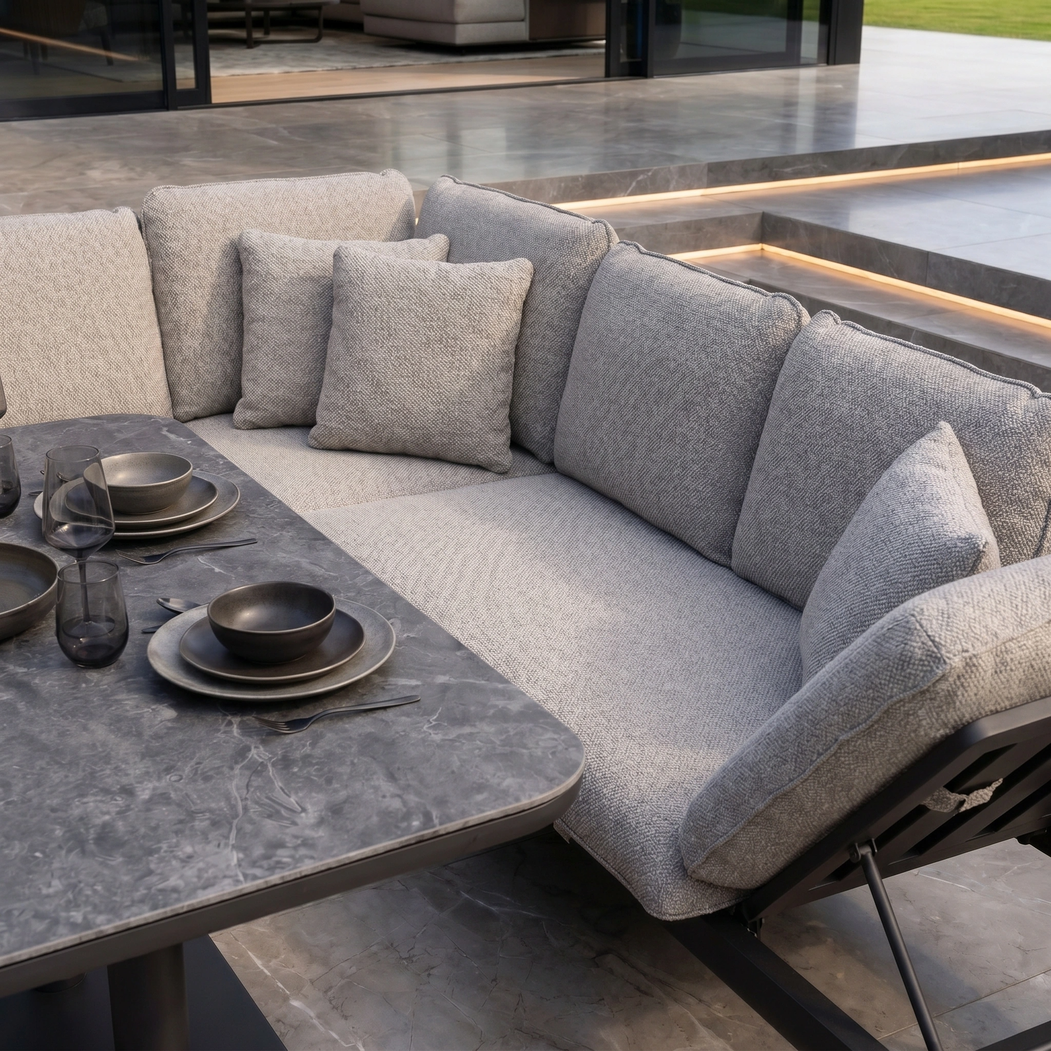 The Como Corner Sofa Set with Altura Rising Table in Truffle, styled with black plates and glasses, creates the perfect outdoor luxury furniture arrangement.