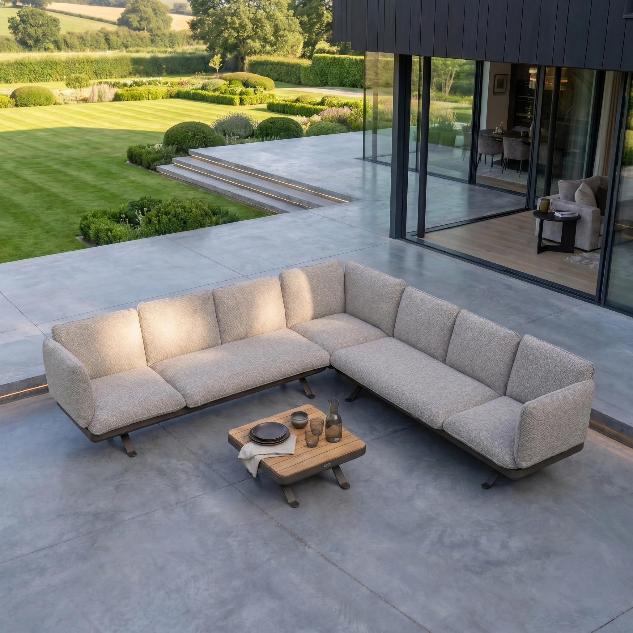 Como Corner Sofa Set in Truffle paired with a wooden coffee table on a spacious patio overlooking a manicured garden, creating the perfect spot for modular garden furniture enthusiasts.