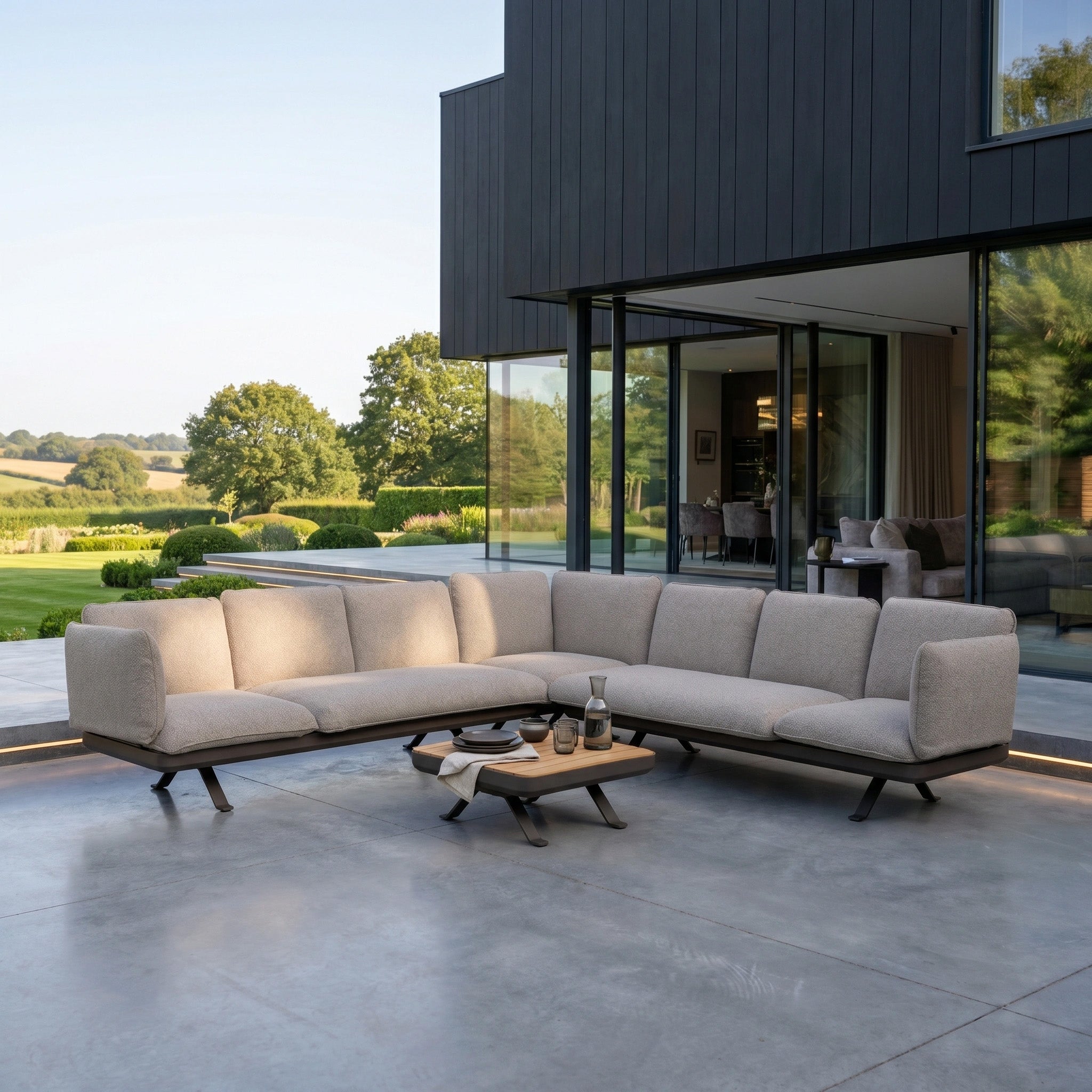 Modern patio featuring the Como Corner Sofa Set in Truffle and coffee table beside a glass-walled house—ideal for those seeking modular garden furniture with luxury outdoor sofa comfort.
