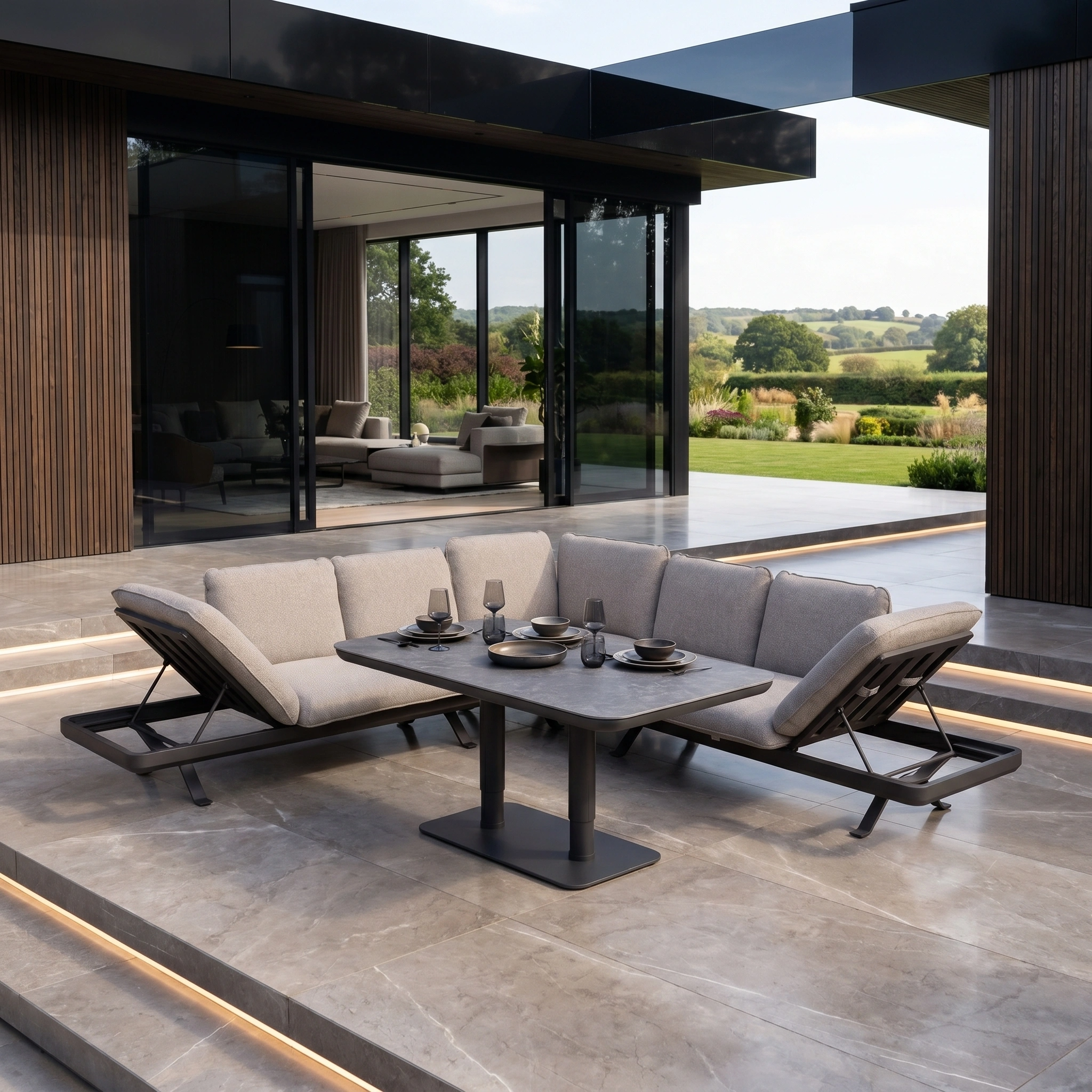 Modern patio with luxury outdoor furniture: the Como Corner Sofa Set with Altura Rising Table in Truffle, set against a scenic garden backdrop.