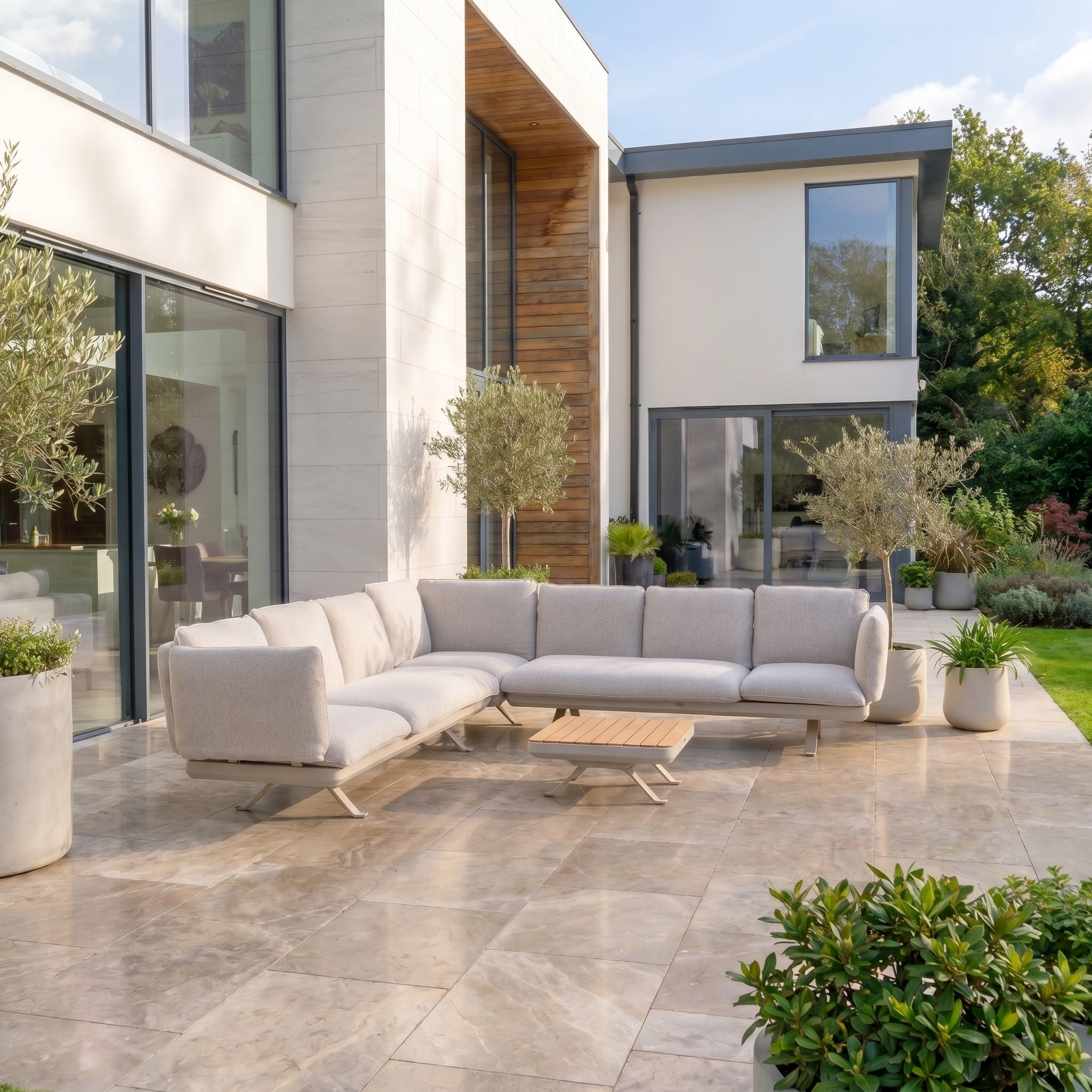 Modern patio with a Como Corner Sofa Set in Oatmeal, small wooden table, and potted plants by a contemporary house—perfect for relaxing with this modular outdoor furniture.