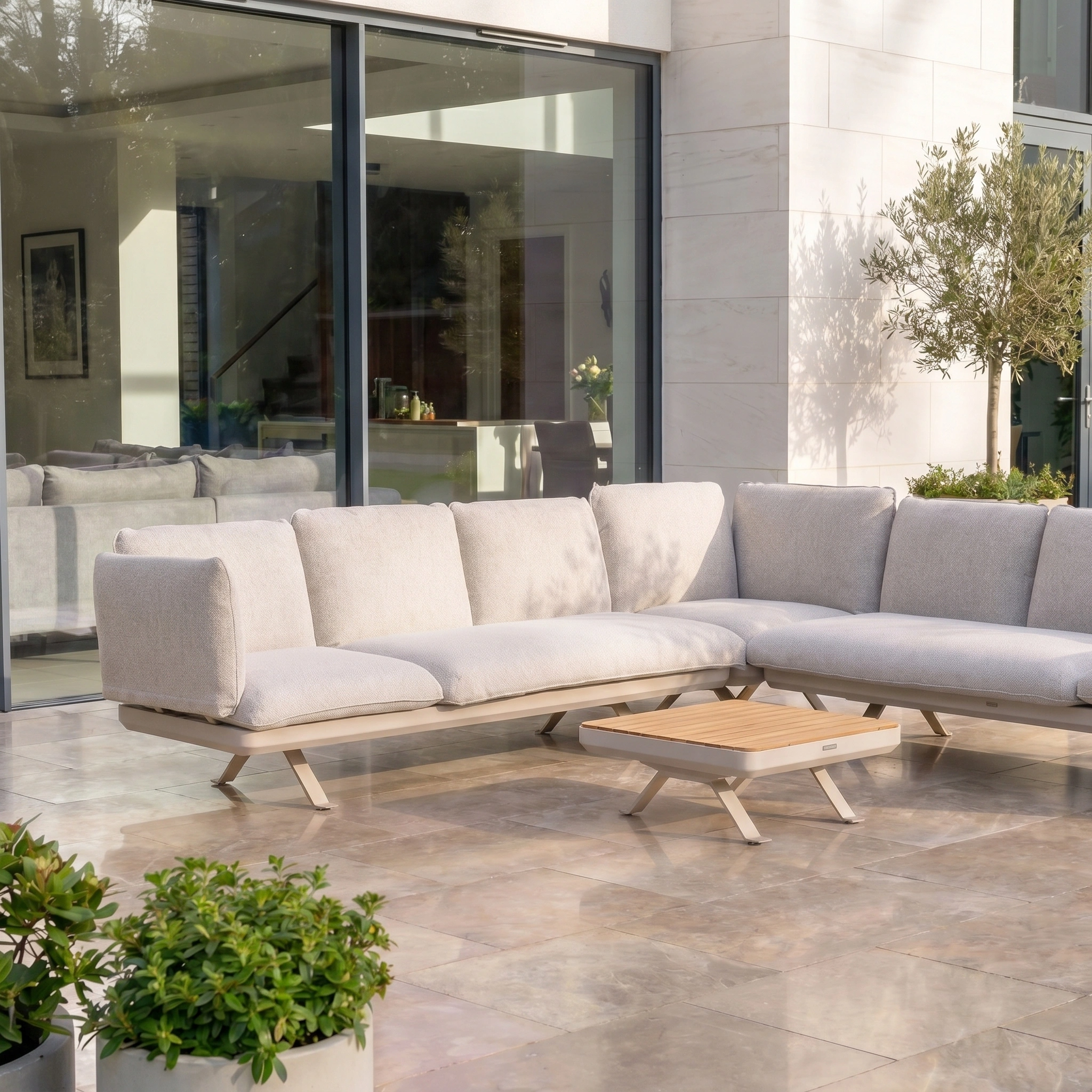 Modern outdoor patio showcasing the Como Corner Sofa Set in Oatmeal, a modular luxury sectional paired with a wooden coffee table on tiled flooring.