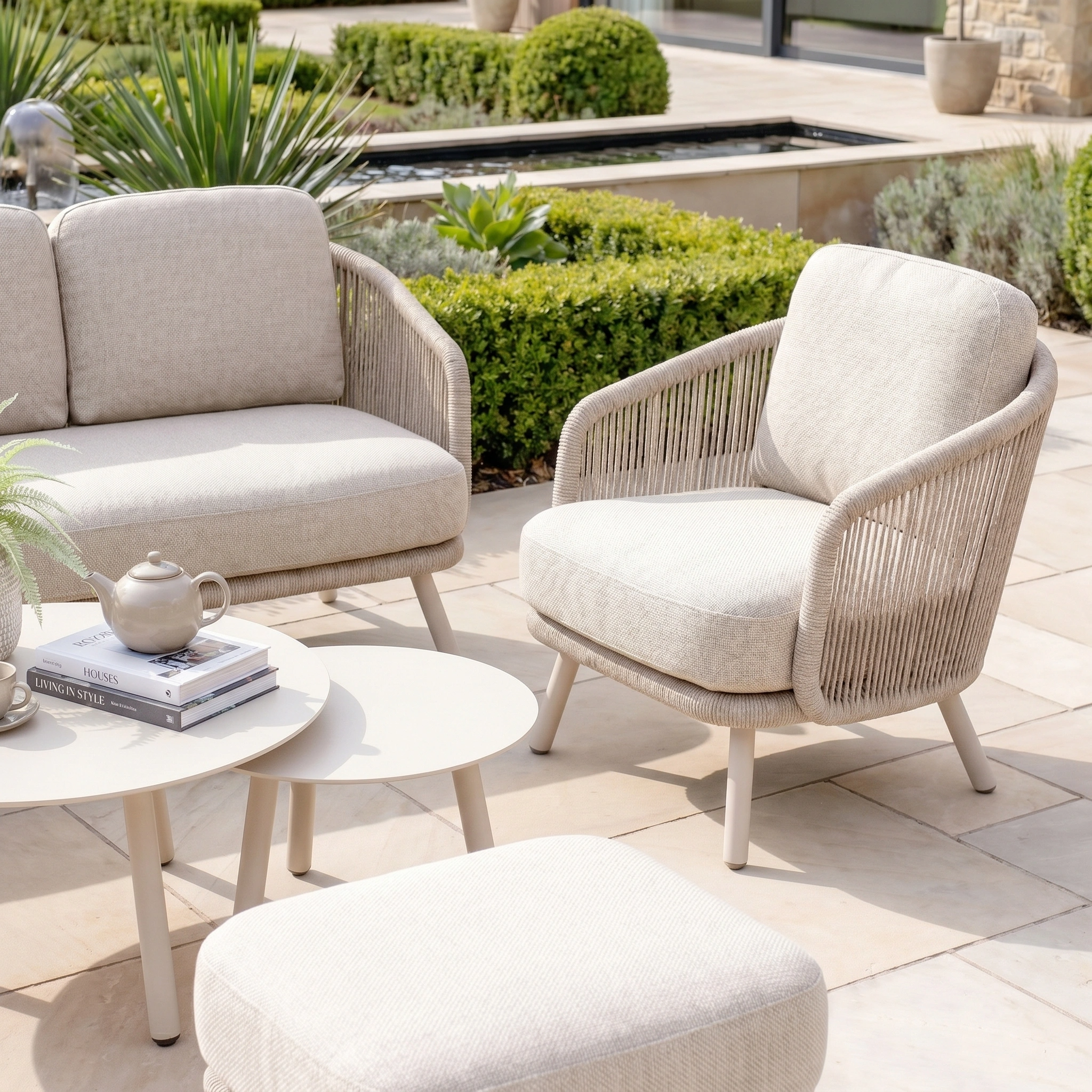 The Dekota 3 Seat Rope Sofa Set in Fawn includes beige rope-back seating, white solution-dyed olefin cushions, coffee tables, and a footstool—perfect for patios.