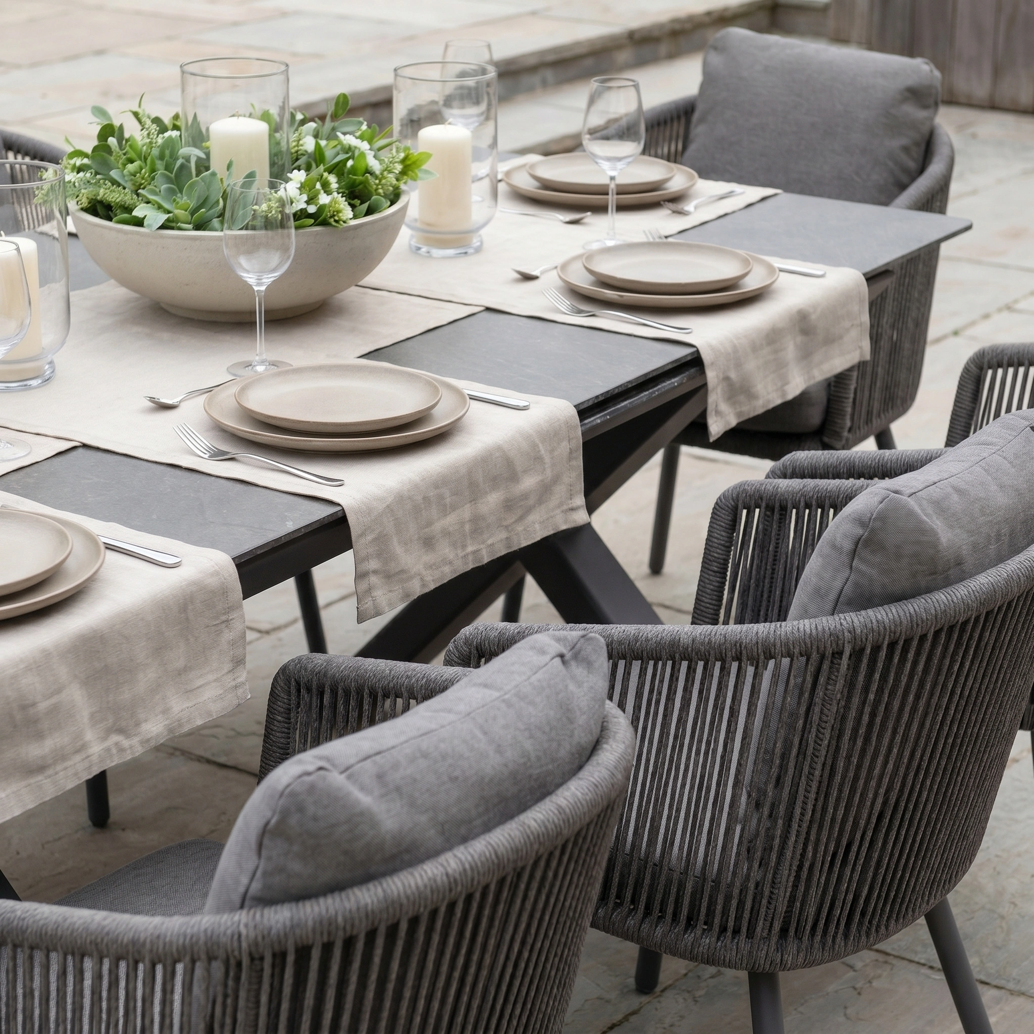 The Dekota 6 Seat Rope Dining Set with Albatross Extending Table in Charcoal is perfect for outdoor dining, styled with neutral plates, glasses, candles, and a green plant centerpiece.