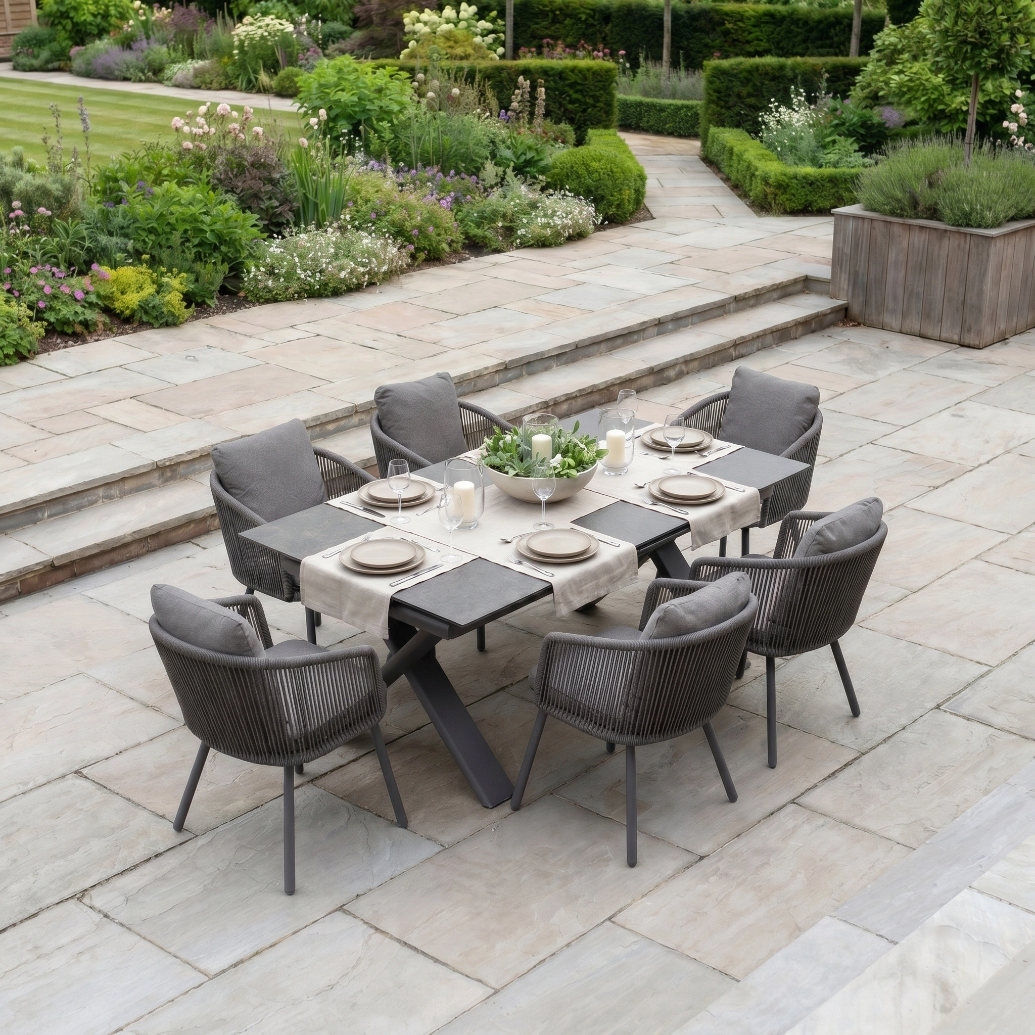 Outdoor dining table set for six on a stone patio with garden views, featuring the Dekota 6 Seat Rope Dining Set with Albatross Extending Table in Charcoal—ideal for gatherings in your outdoor oasis.