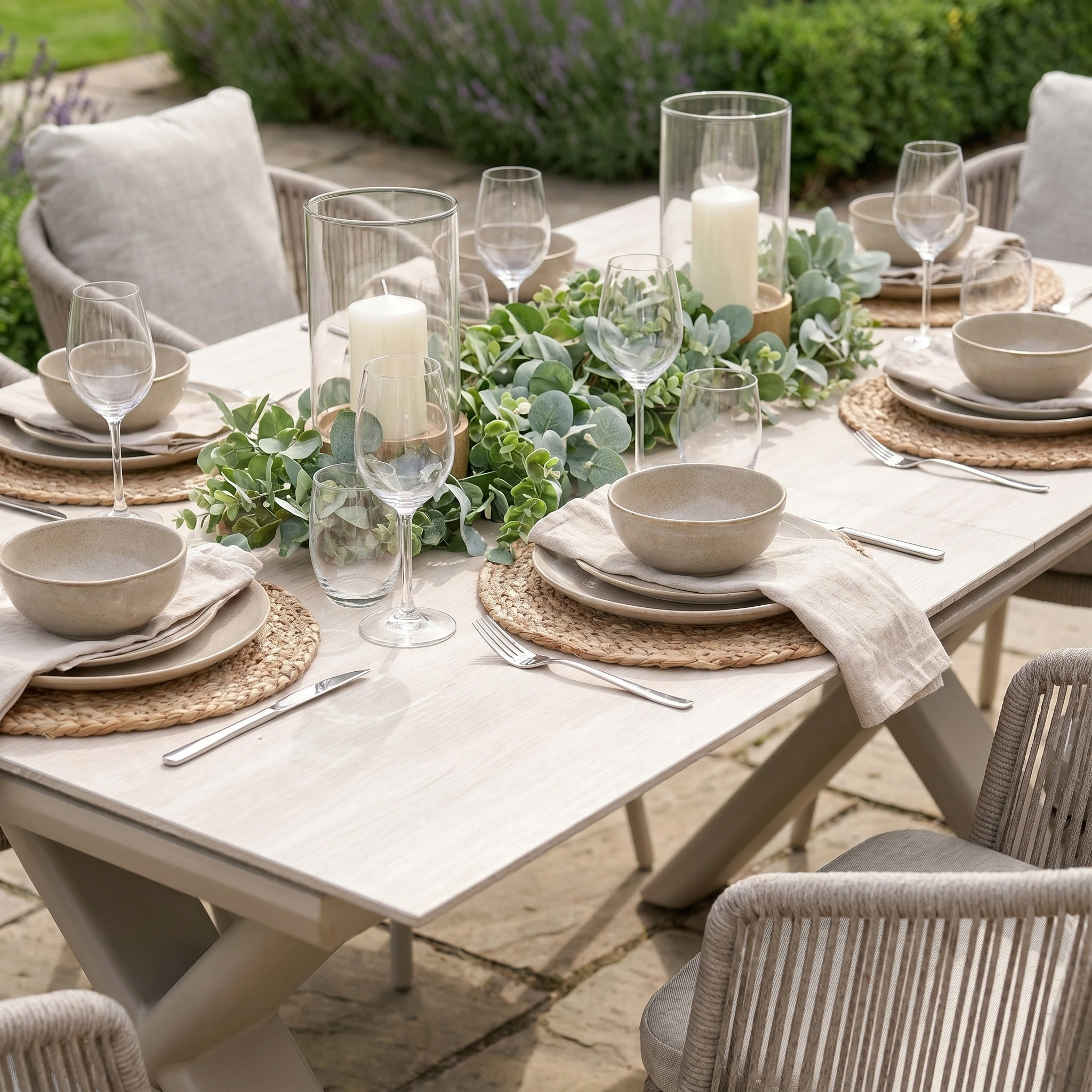 Create memorable al fresco gatherings with the Dekota 6 Seat Rope Dining Set with Albatross Extending Table in Fawn, featuring elegant stoneware, wine glasses, candles, and a eucalyptus garland for a stylish outdoor dining ambiance.