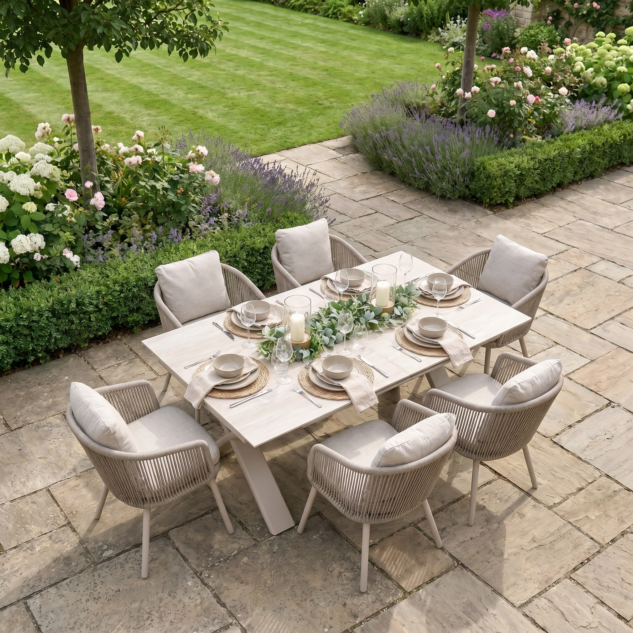Enjoy outdoor dining for six on a stone patio with the elegant Dekota 6 Seat Rope Dining Set with Albatross Extending Table in Fawn, surrounded by lush garden and a green lawn.