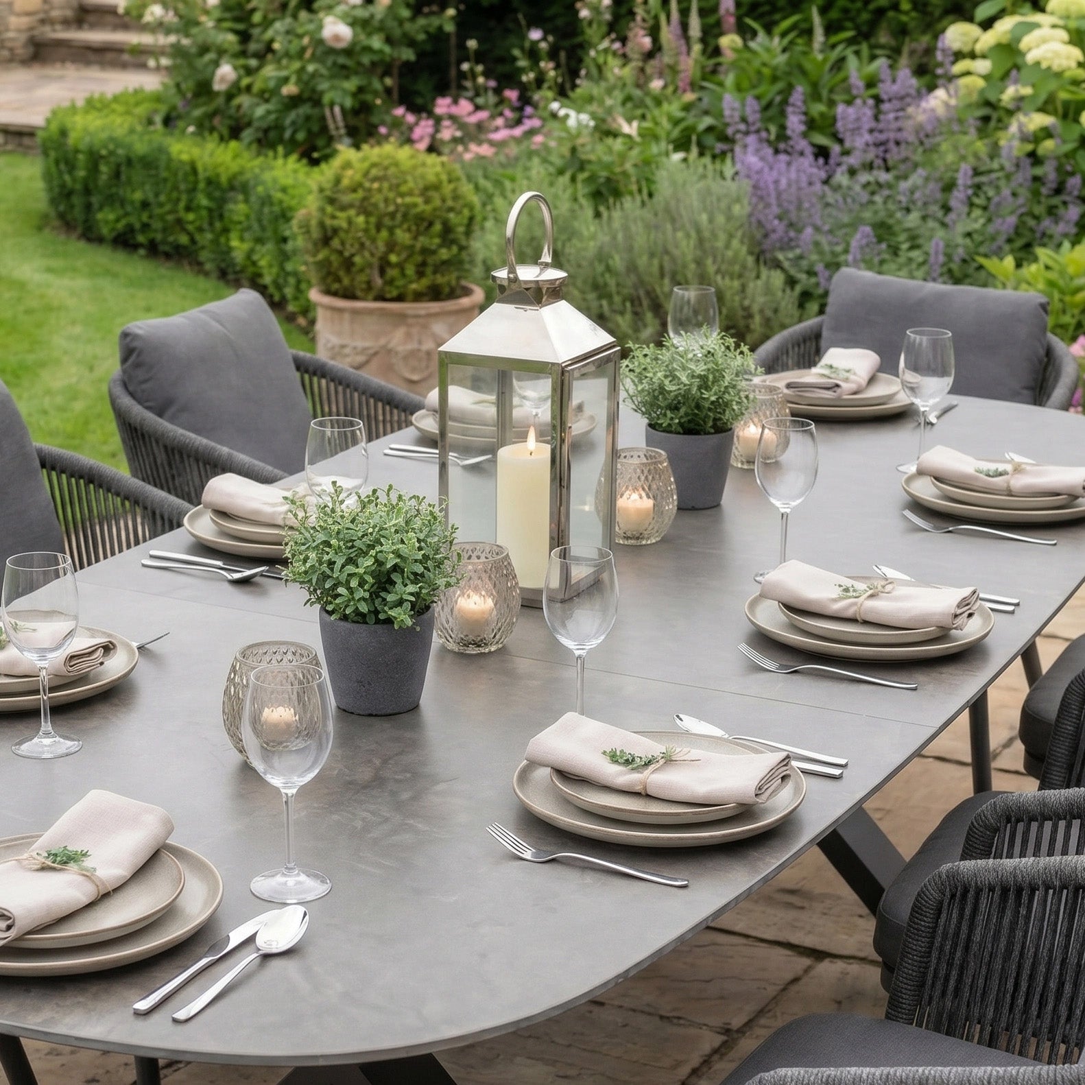 The Dekota 8 Seat Oval Rope Dining Set features an Albatross extending table with a durable sintered stone top in charcoal, perfect for garden dining with plates, napkins, wine glasses, candles, and potted plants.