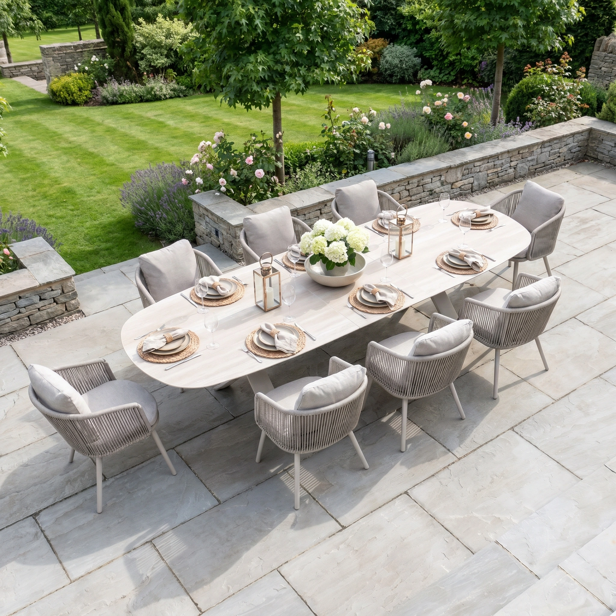 Enjoy alfresco meals with the Dekota 8 Seat Oval Rope Dining Set, featuring an Albatross Extending Table in Fawn, perfect for stone patios and surrounded by lush garden greenery and flowers.