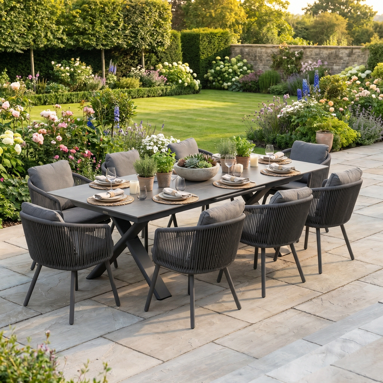 The Dekota 8 Seat Rope Dining Set with Albatross Extending Table in Charcoal provides stylish outdoor dining for eight on your patio, perfect for enjoying meals amid a lush garden with blooming flowers.