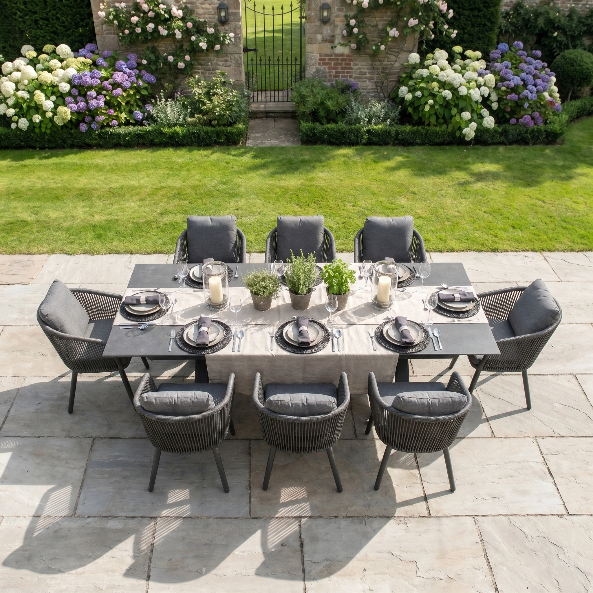 The Dekota 8 Seat Rope Dining Set with Albatross Extending Table in Charcoal offers stylish, durable outdoor dining for eight—perfect for gatherings on a stone patio amid blooming flowers and greenery all season long.
