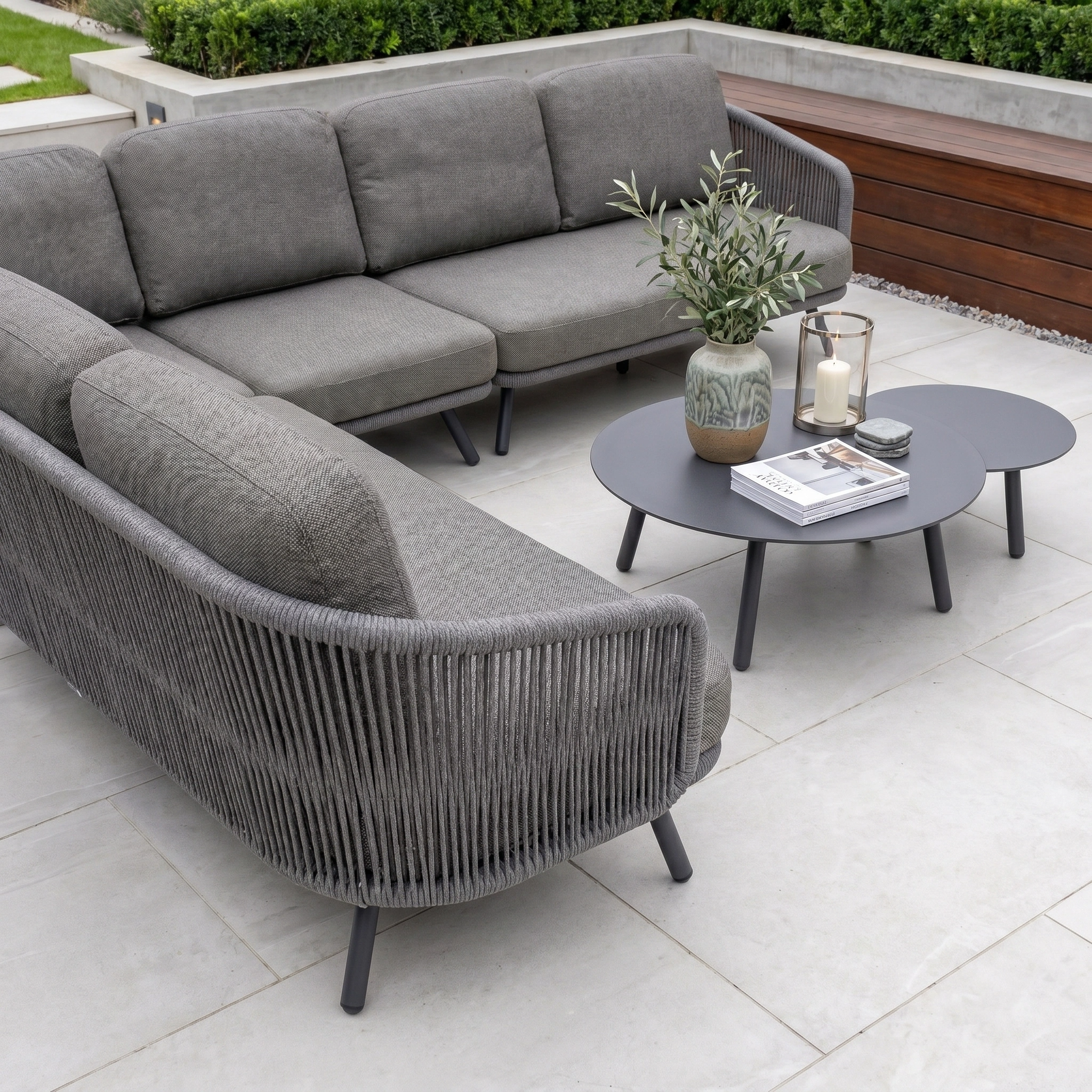 Dekota Large Corner Sofa Set in Charcoal with coffee tables, a vase, and a candle—perfect outdoor furniture for relaxing in style.