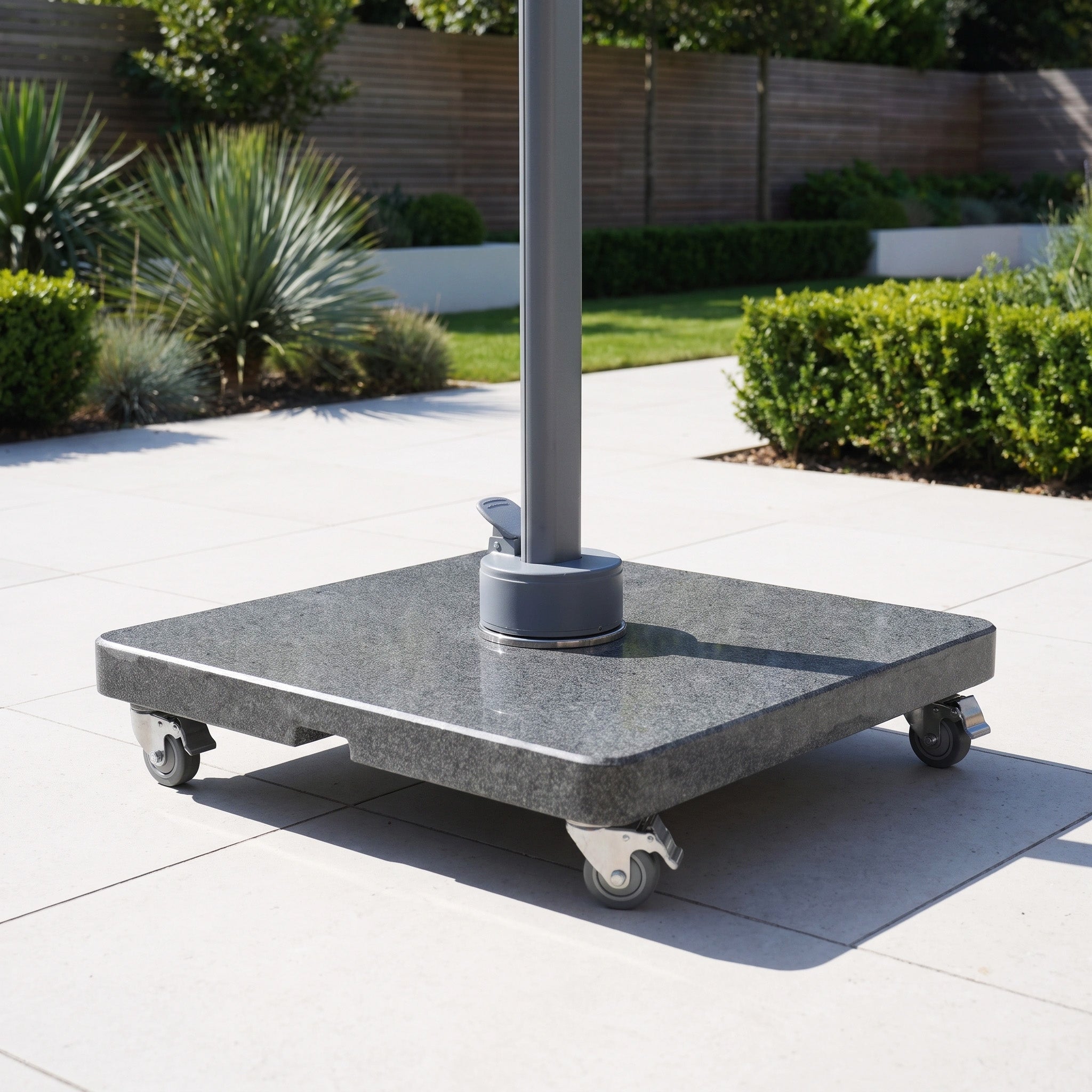 The Granite 120kg Cantilever Parasol Base With Wheels on a tiled patio, surrounded by plants and bushes in the background.