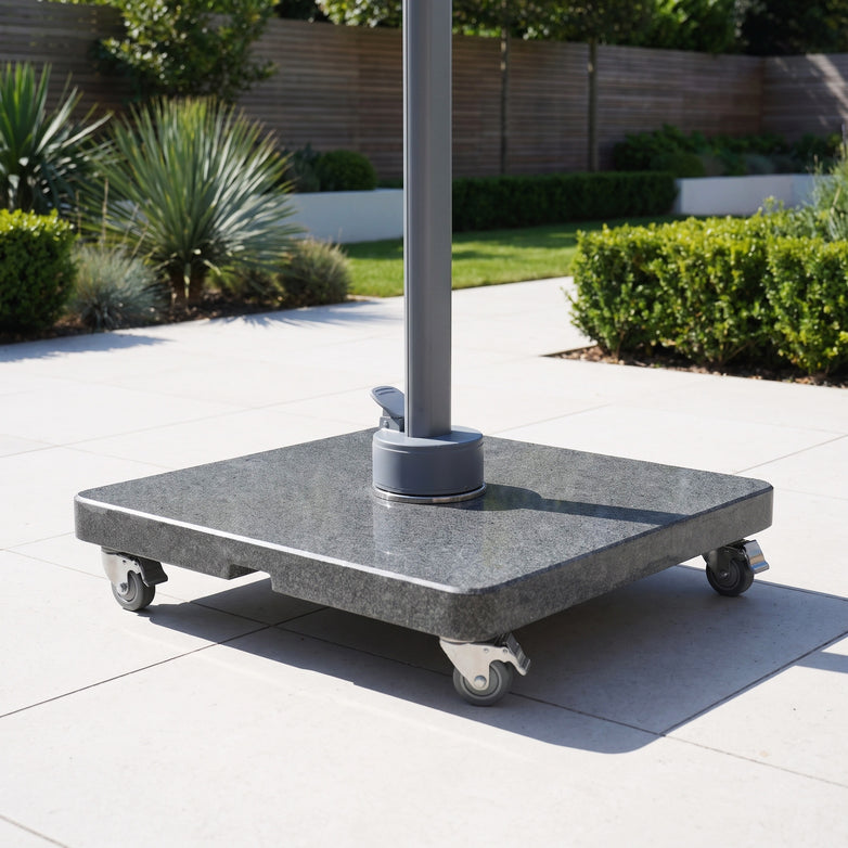 The Granite 120kg Cantilever Parasol Base With Wheels on a tiled patio, surrounded by plants and bushes in the background.
