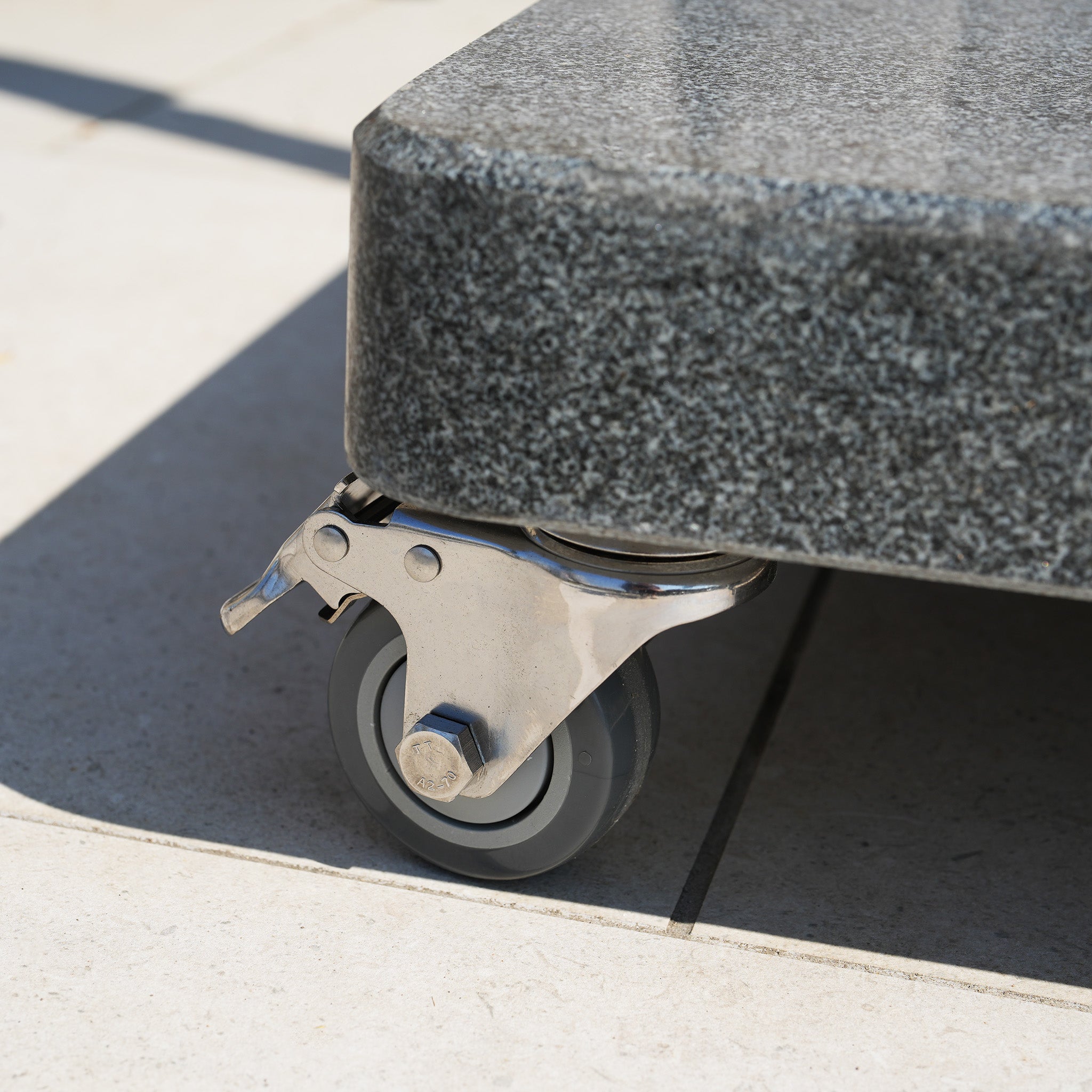 Close-up of a metal caster wheel attached to the corner of the Granite 120kg Cantilever Parasol Base With Wheels on tile flooring, highlighting its sturdy design and easy mobility—ideal for outdoor settings.