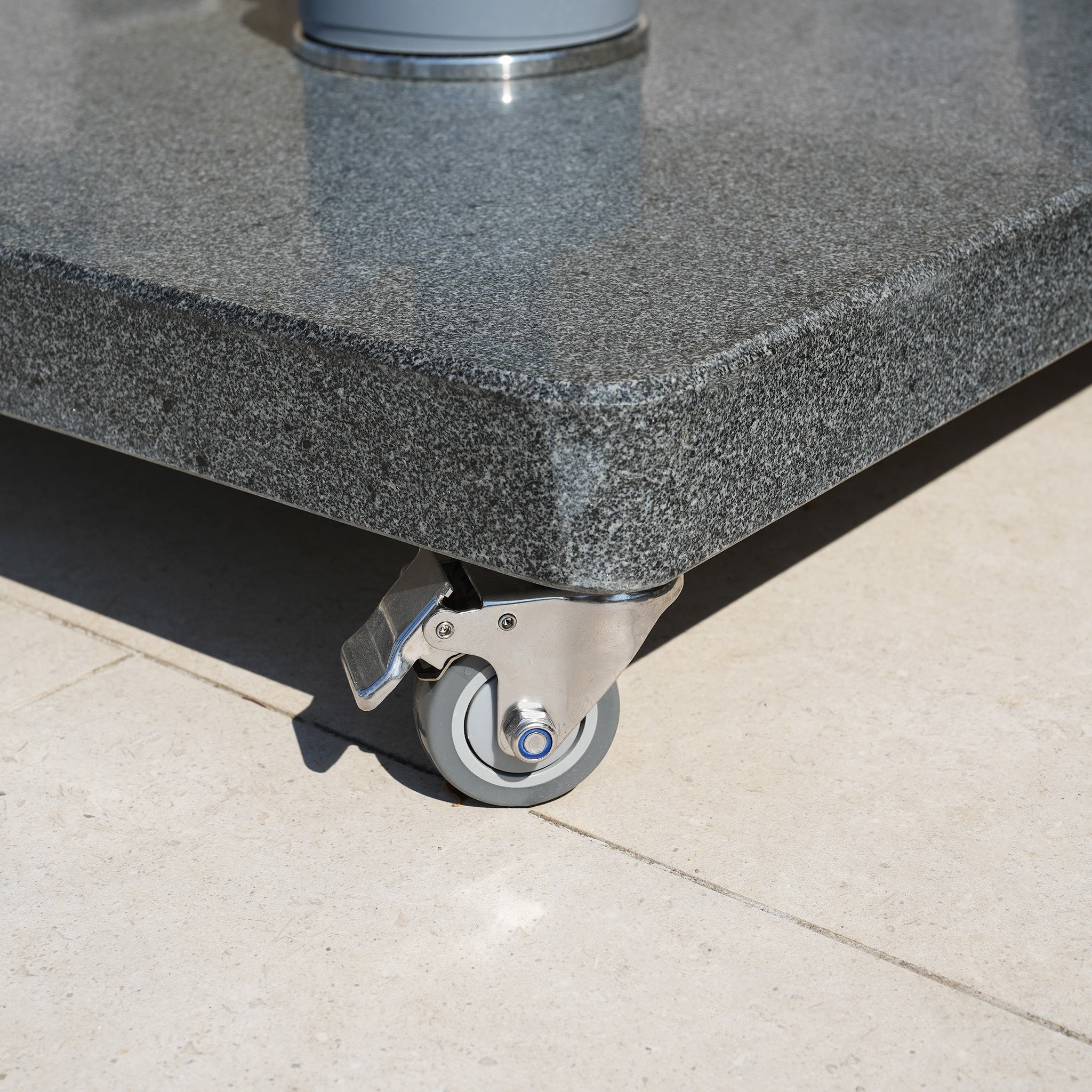 A close-up of a Granite 120kg Cantilever Parasol Base With Wheels featuring a gray caster wheel on a tiled floor.