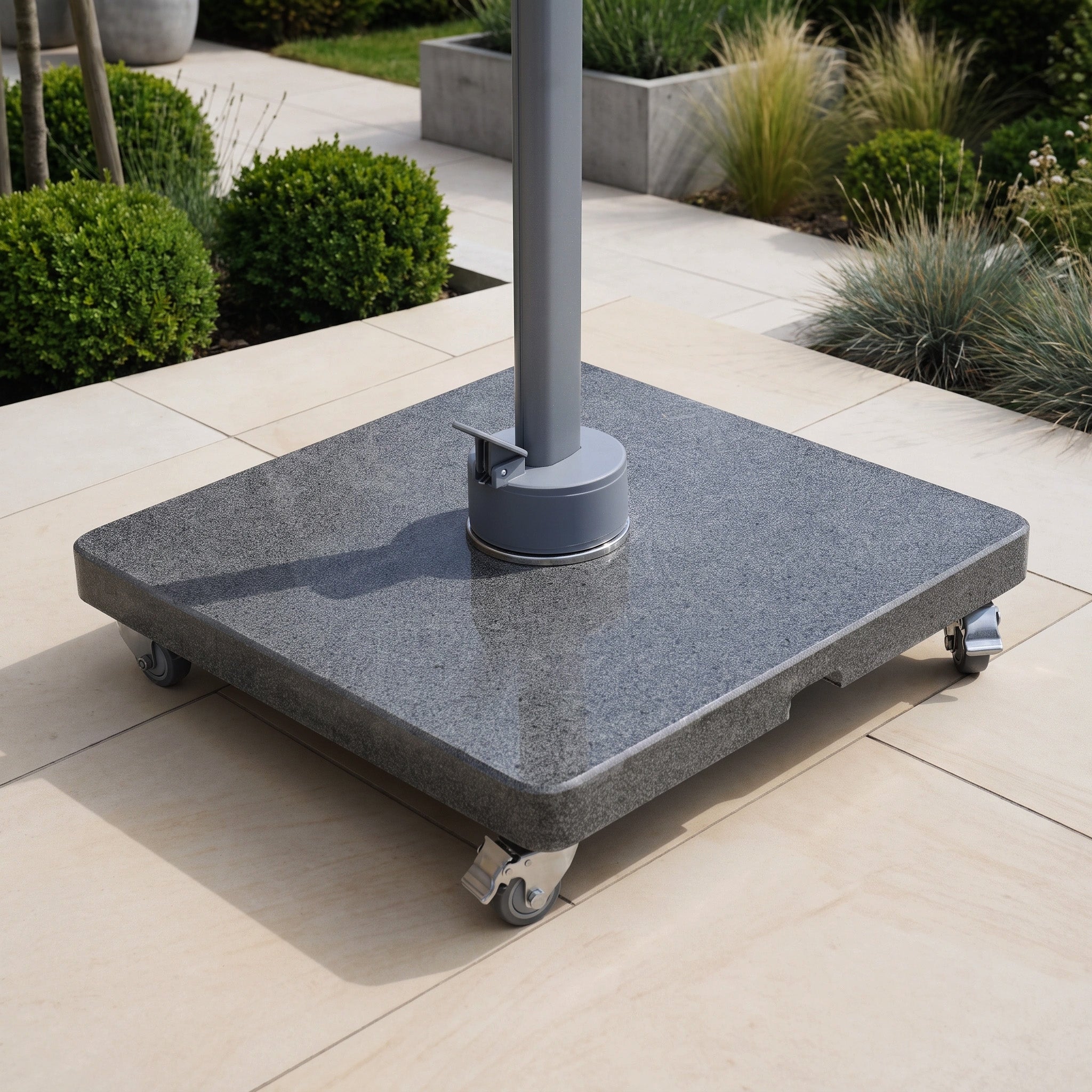 The Granite 120kg Cantilever Parasol Base With Wheels sits on a light patio, surrounded by green bushes and ornamental grass—making it an ideal choice for effortless mobility and stylish support for your cantilever parasol.