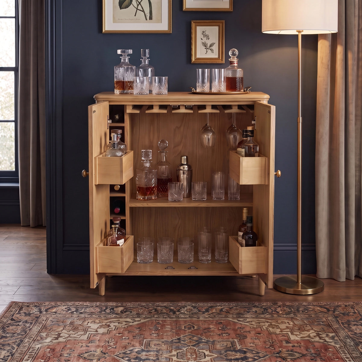 The Hadley Herringbone Drinks Cabinet in Natural stands open in a warmly lit room, displaying its elegant collection of glasses, decanters, and bottles. This natural oak cabinet is the perfect statement piece for any home bar setup, combining style and functionality with timeless charm.