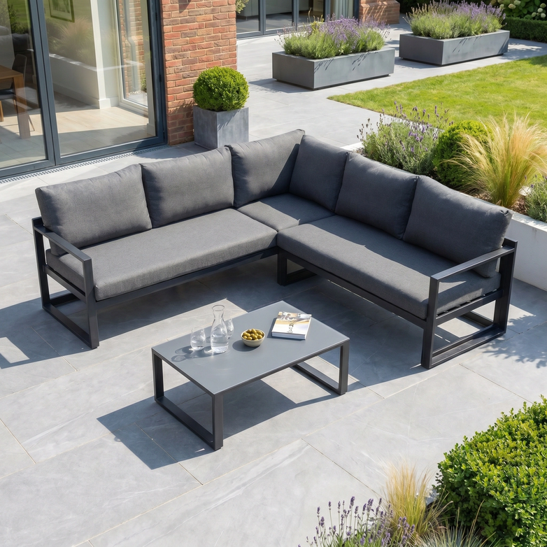 The Havana Corner Group Set with Reclining Feature and Coffee Table in Charcoal features gray cushions, perfect for relaxing outdoors on a tiled terrace surrounded by greenery.
