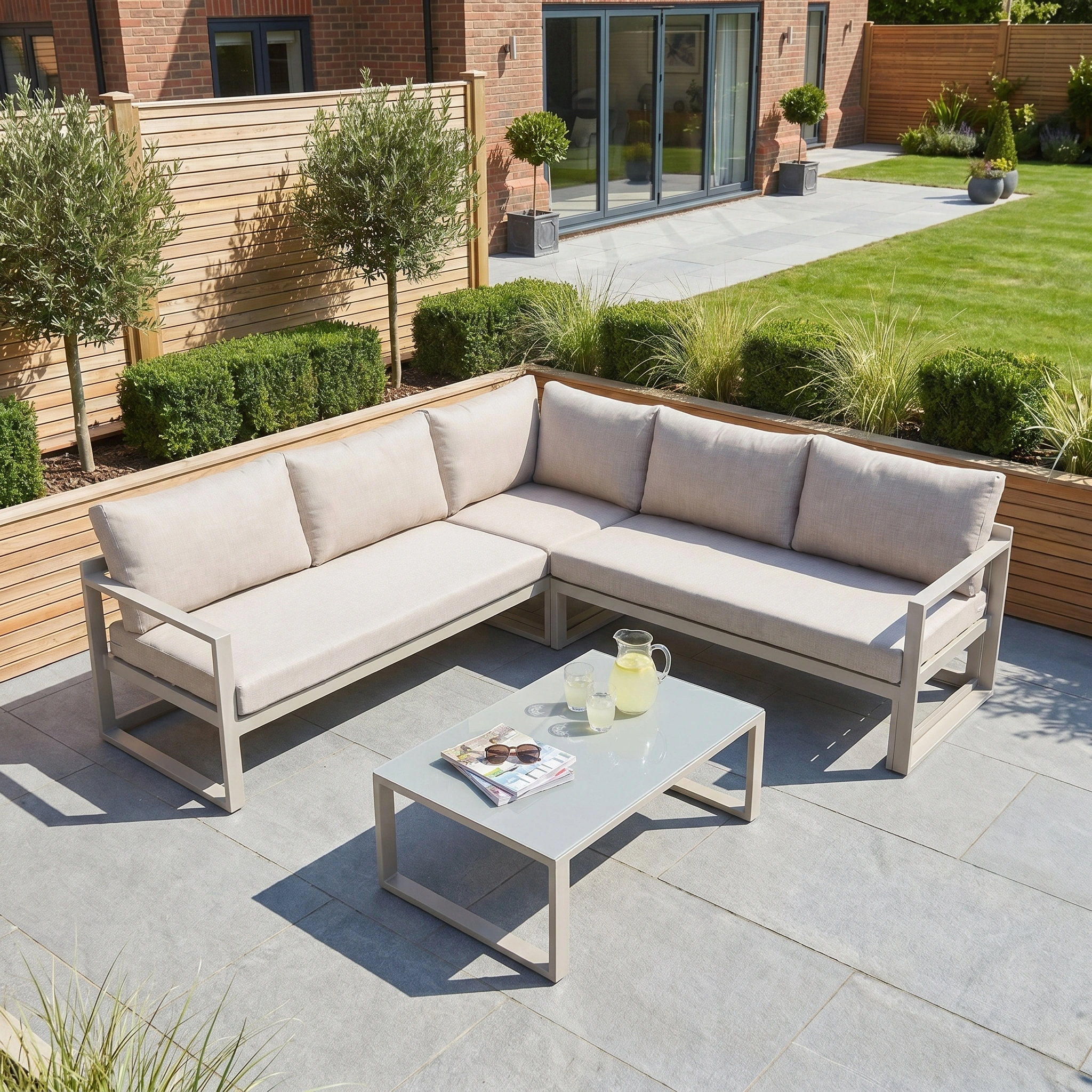 Modern outdoor patio with the Havana Corner Group Set in Latte, featuring a reclining corner sofa and coffee table, plus magazines and a pitcher of lemonade.