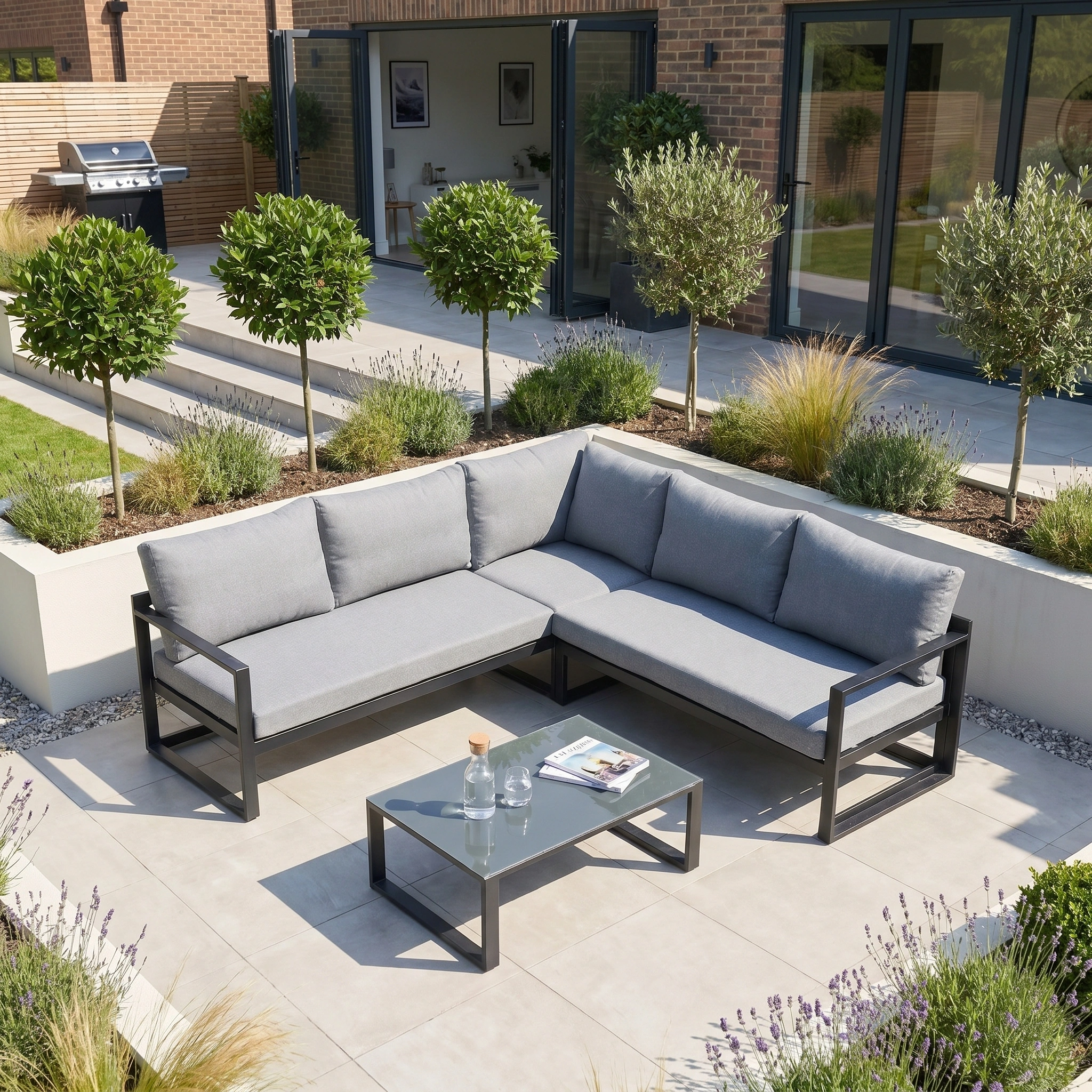 A modern outdoor patio with the Havana Corner Group Set in Washed Grey, featuring reclining seats and a sleek coffee table, surrounded by lush greenery on a sunny day.