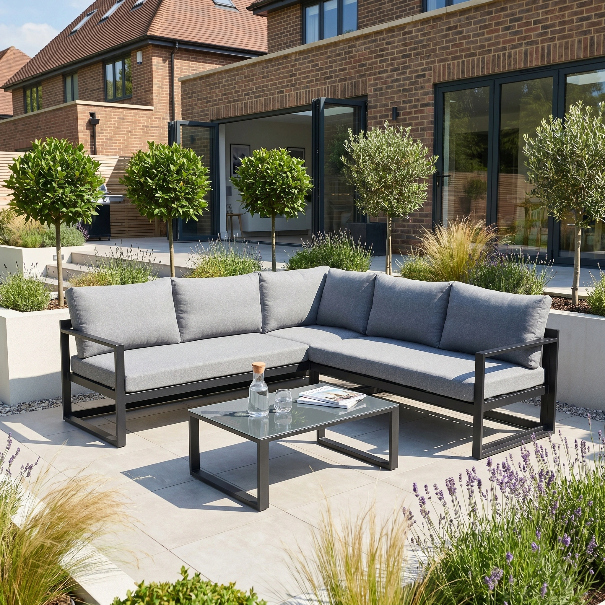 Modern outdoor patio with a Havana Corner Group Set featuring a reclining design and coffee table in washed grey, surrounded by potted trees in a landscaped garden.