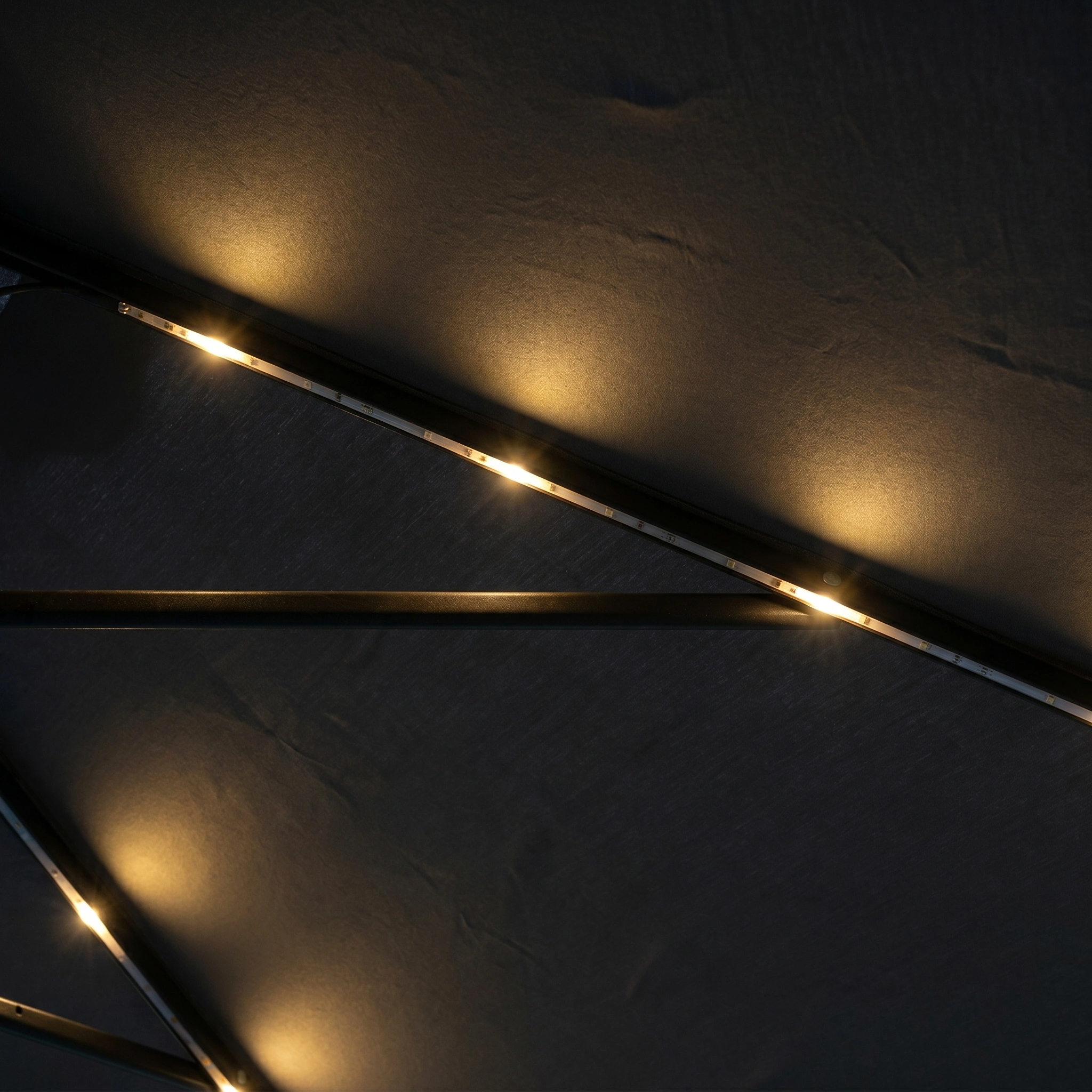 Soft yellow LED lights brighten the dark metal frame of the Hera 3m Round Cantilever Parasol with LED Lighting in Grey, creating a warm nighttime glow.