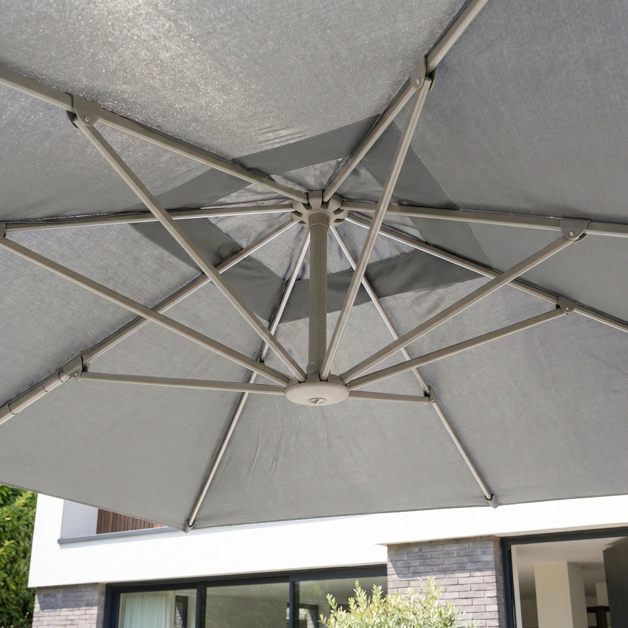 View from beneath the Hera 2.7m Square Cantilever Parasol with LED Lighting in Charcoal, showcasing its robust metal spokes and a modern building in the background.