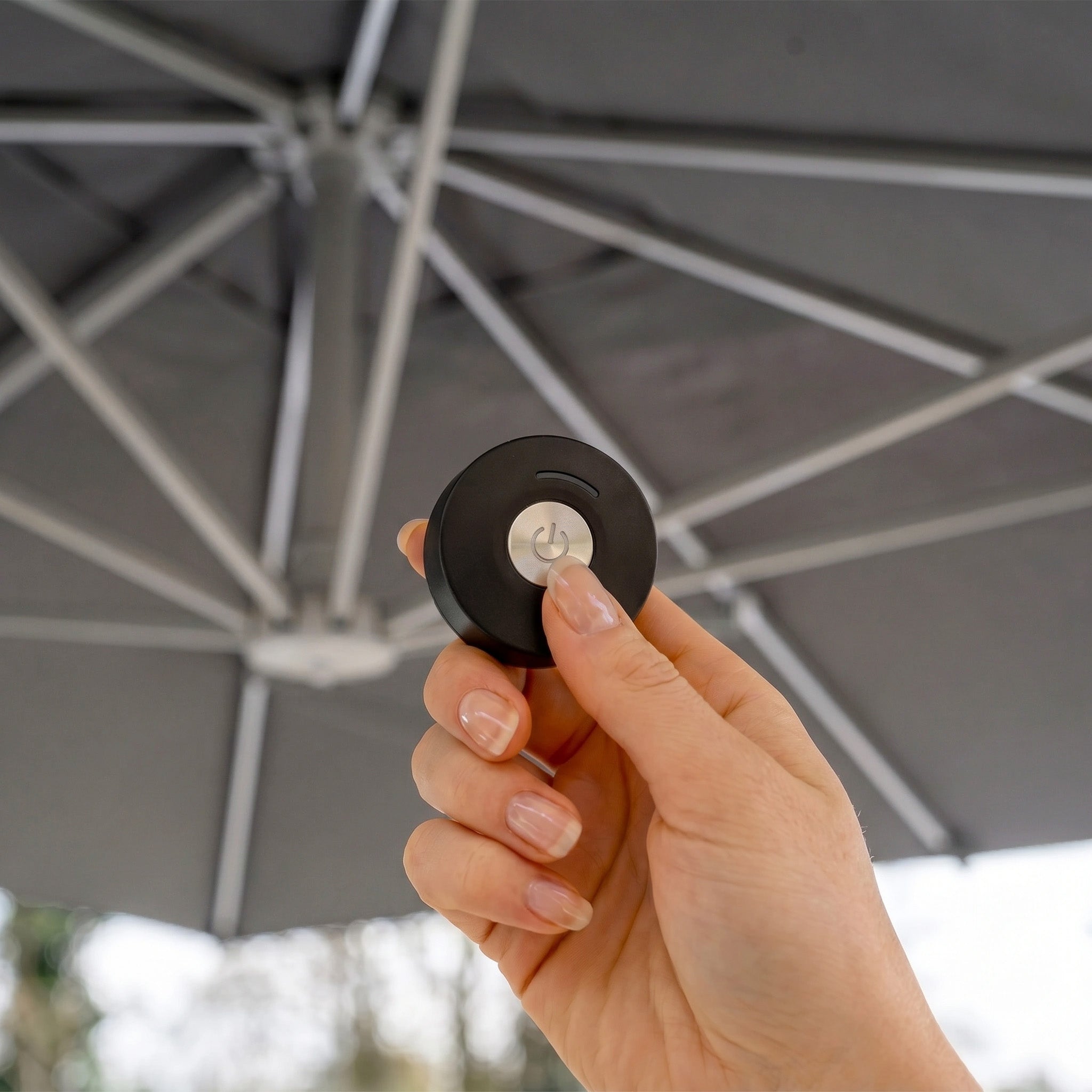 A hand holds a remote under the Hera 3m Round Cantilever Parasol with LED Lighting in Grey, featuring an impressive UV50+ canopy.