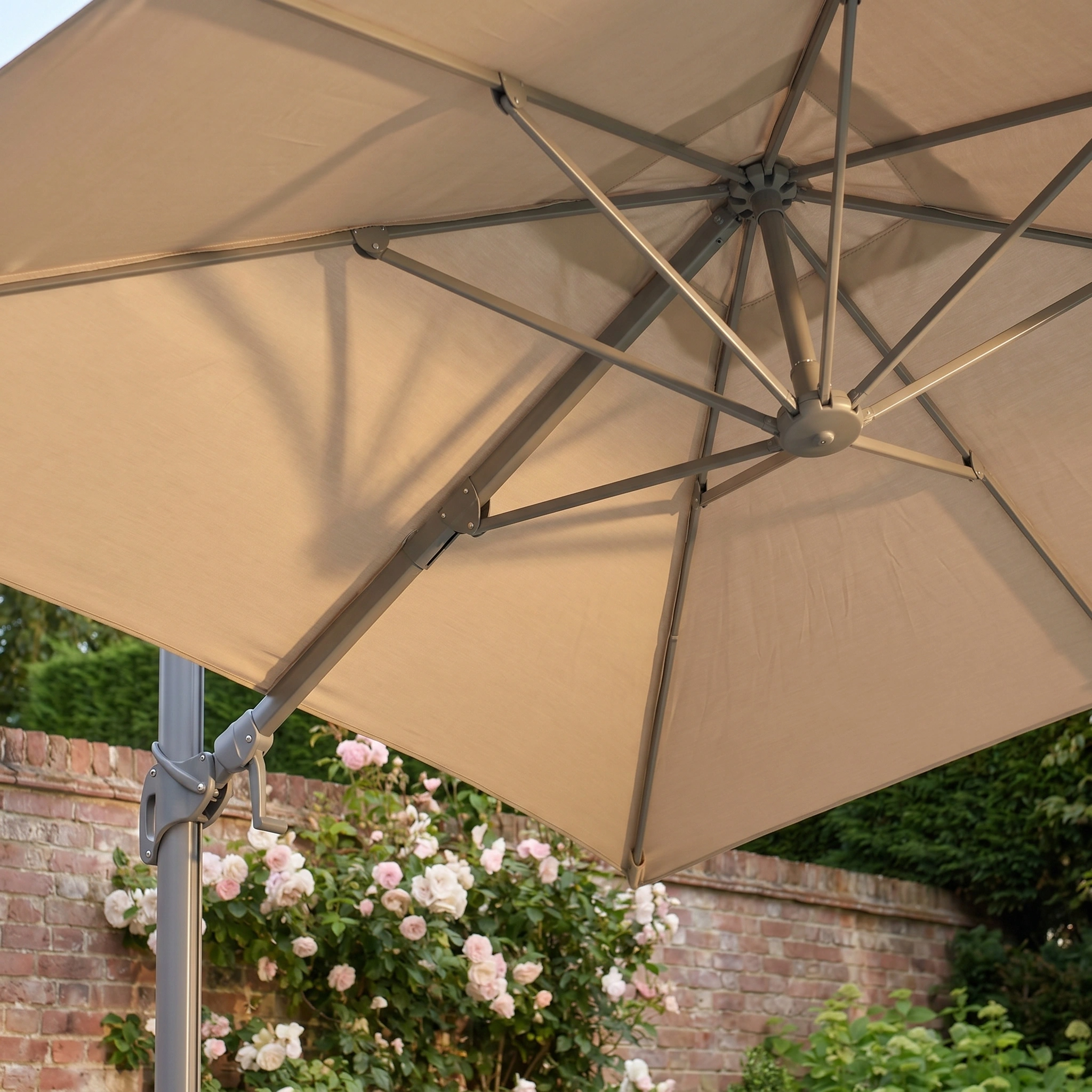 The Hera 3m x 2m Rectangular Cantilever Parasol with LED Lighting in Beige provides shade for blooming pink roses by a brick wall, thanks to its sturdy metal frame and UV-protective canopy.