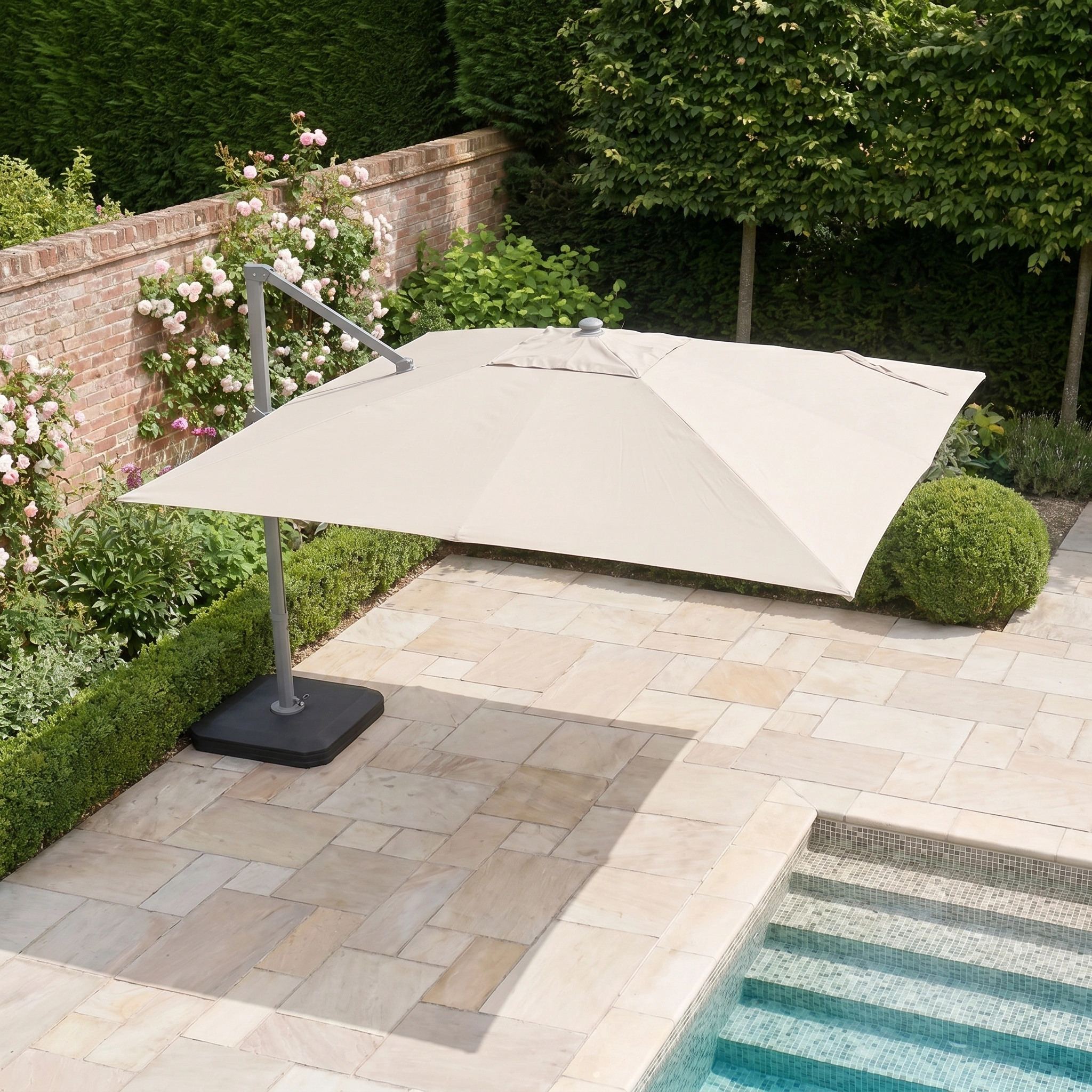 The Hera 3m x 2m Rectangular Cantilever Parasol with LED Lighting in Beige provides stylish shade to a stone poolside area, surrounded by garden plants and a brick wall, offering comfort and elegance.