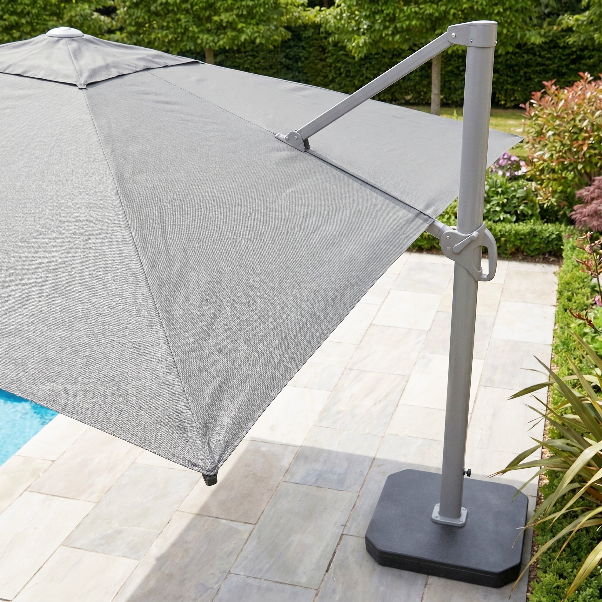 A Hera 3m x 2m Rectangular Cantilever Parasol with LED Lighting in Grey and a UV50+ canopy stands open beside a pool on a tiled patio.