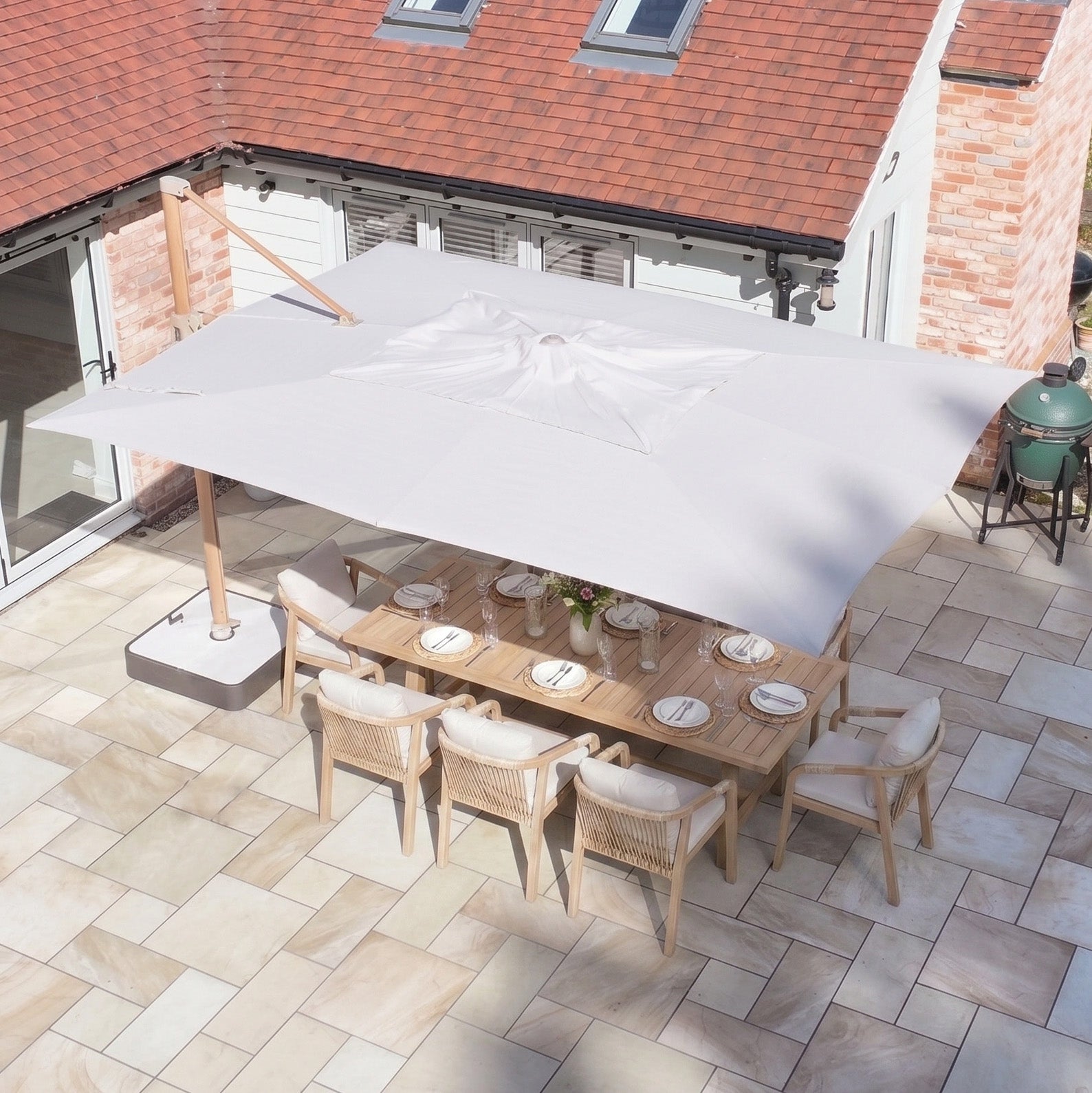 The Finca 4m x 3m Cantilever Parasol in Sand offers outdoor sun protection for an eight-seater dining table on a tiled patio by the house.