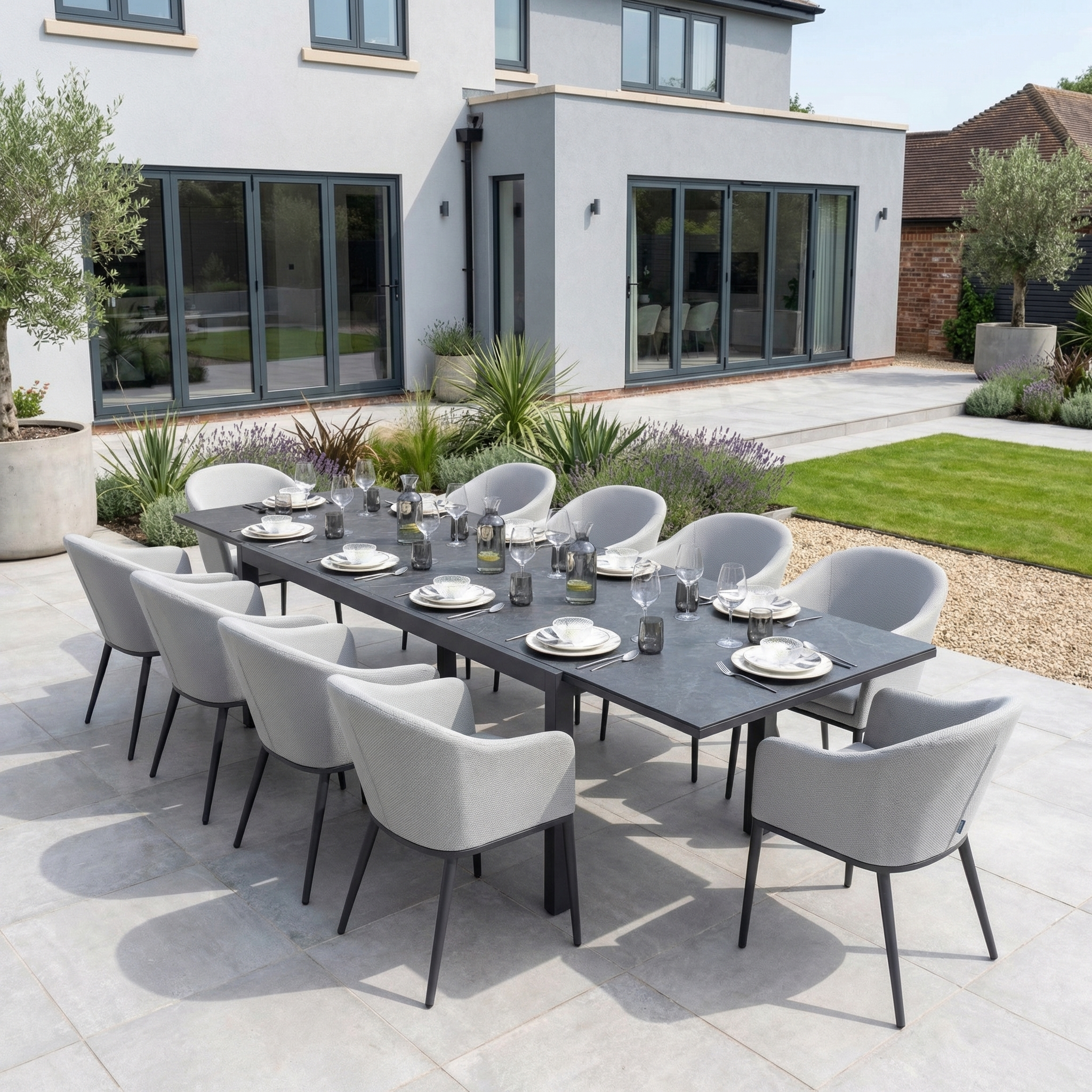 Host twelve guests on your patio with the Luna 10 Seat Outdoor Fabric Extending Ceramic Dining Set in Oyster Grey, shown here with a modern house and garden as the backdrop.