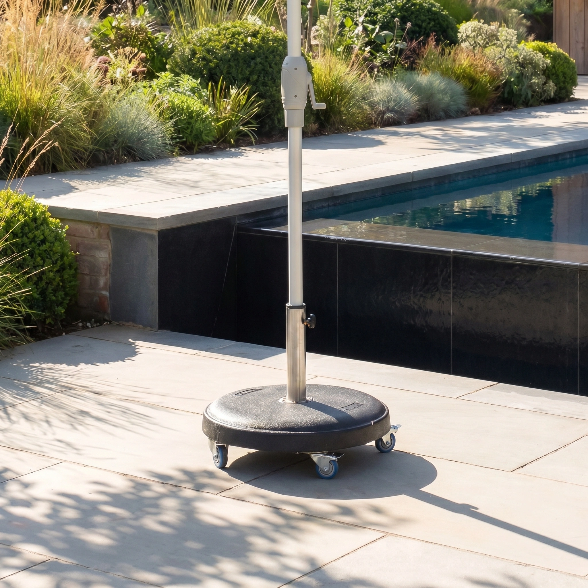 The Zelos 3m x 2m Rectangular Parasol with LED Lighting in Green stands on a wheeled outdoor base on a stone patio by the pool, surrounded by lush greenery.