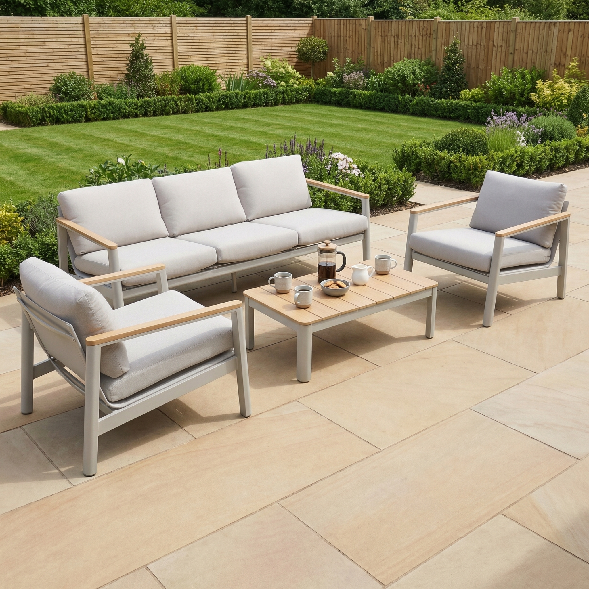 The Cora 3 Seat Sofa Set in Latte, featuring cushioned chairs and an aluminium frame sofa, is arranged around a coffee table on a weather-resistant stone patio in the garden.