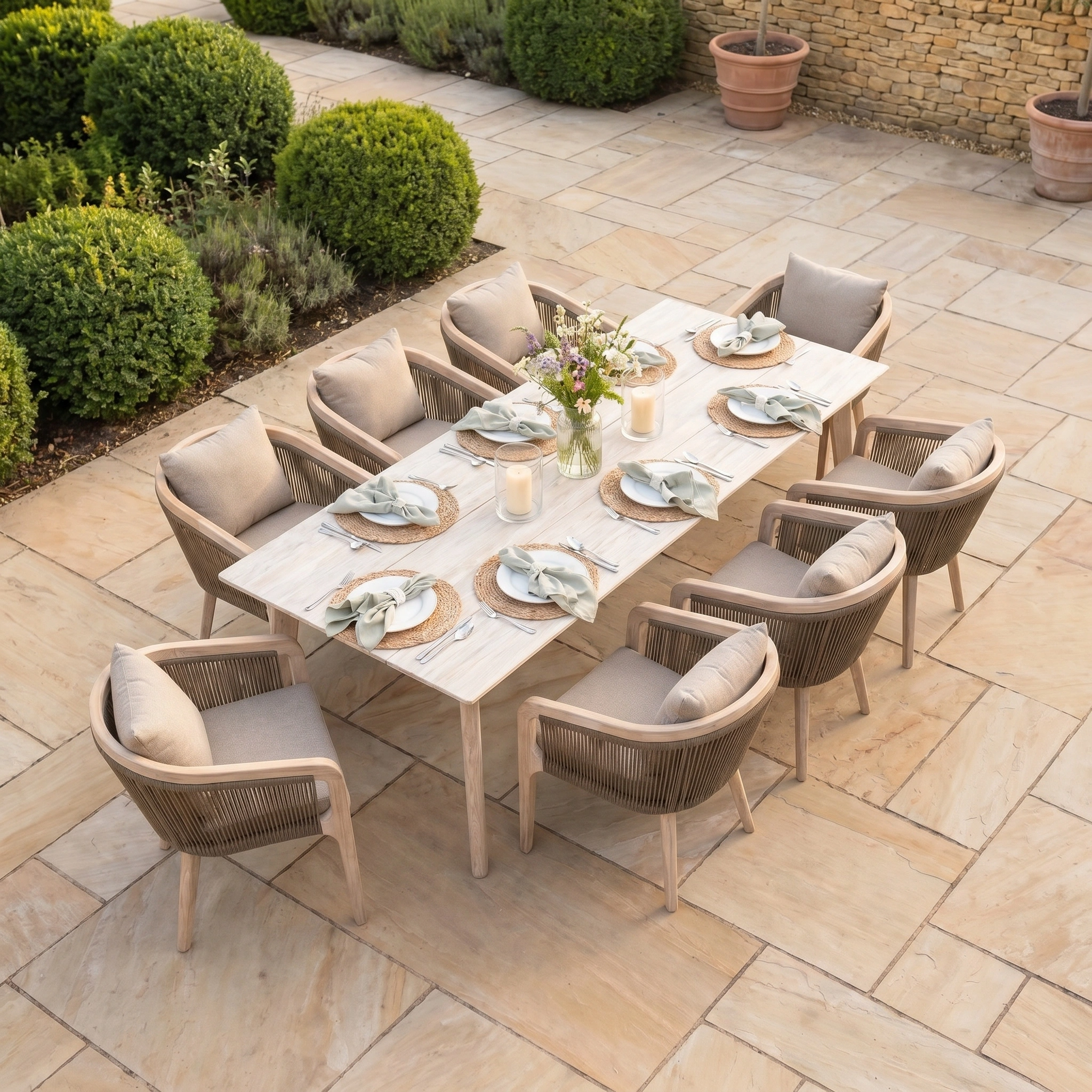 The Evora 8 Seat Rectangular Dining Set in Mocha, featuring a teak table and rope dining chairs, is displayed on a stone patio.