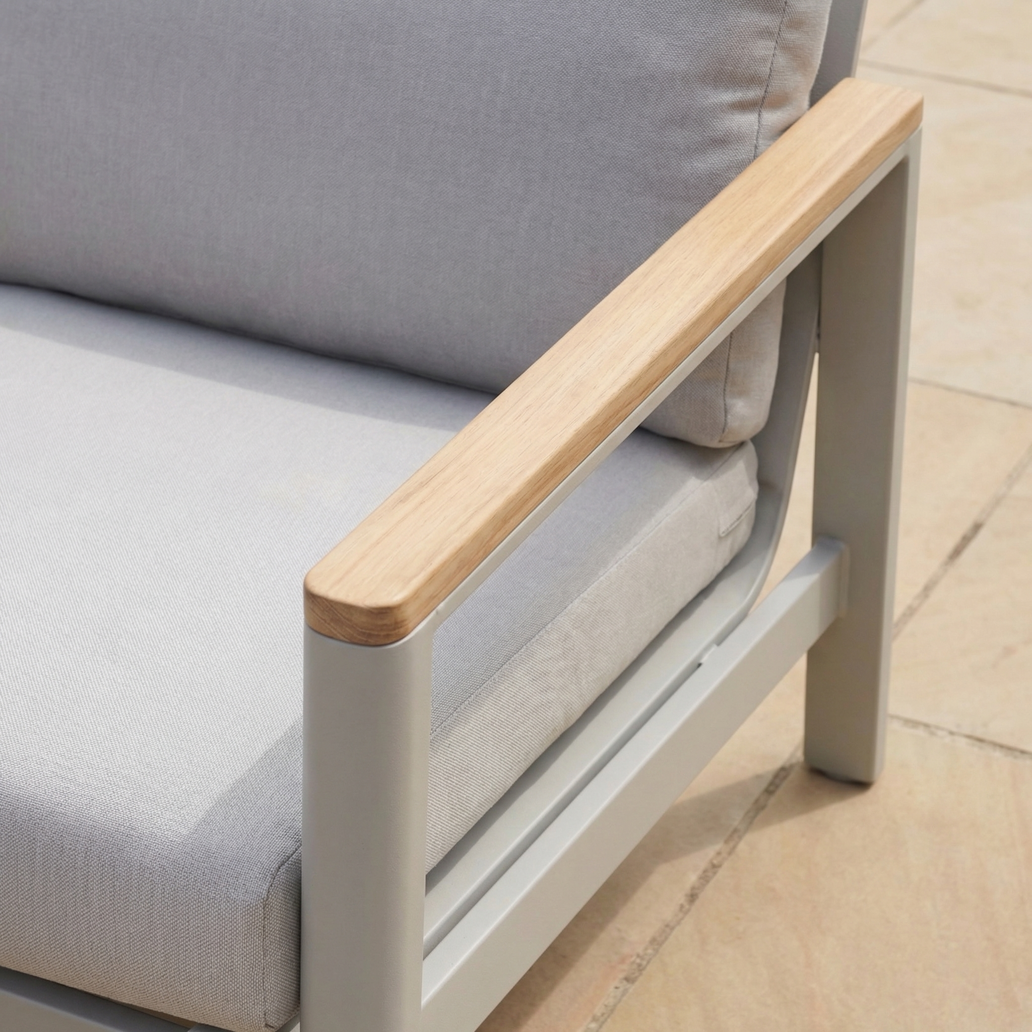 Close-up of the Cora 3 Seat Sofa Set in Latte, featuring light gray cushions, a wooden armrest, and an aluminum frame on a tiled floor—perfect for stylish outdoor spaces.