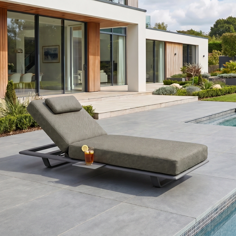 The Hatia Single Sun Lounger with Side Table in Charcoal is a UV resistant outdoor piece, ideal for stylish poolside relaxation on your patio near a modern house.