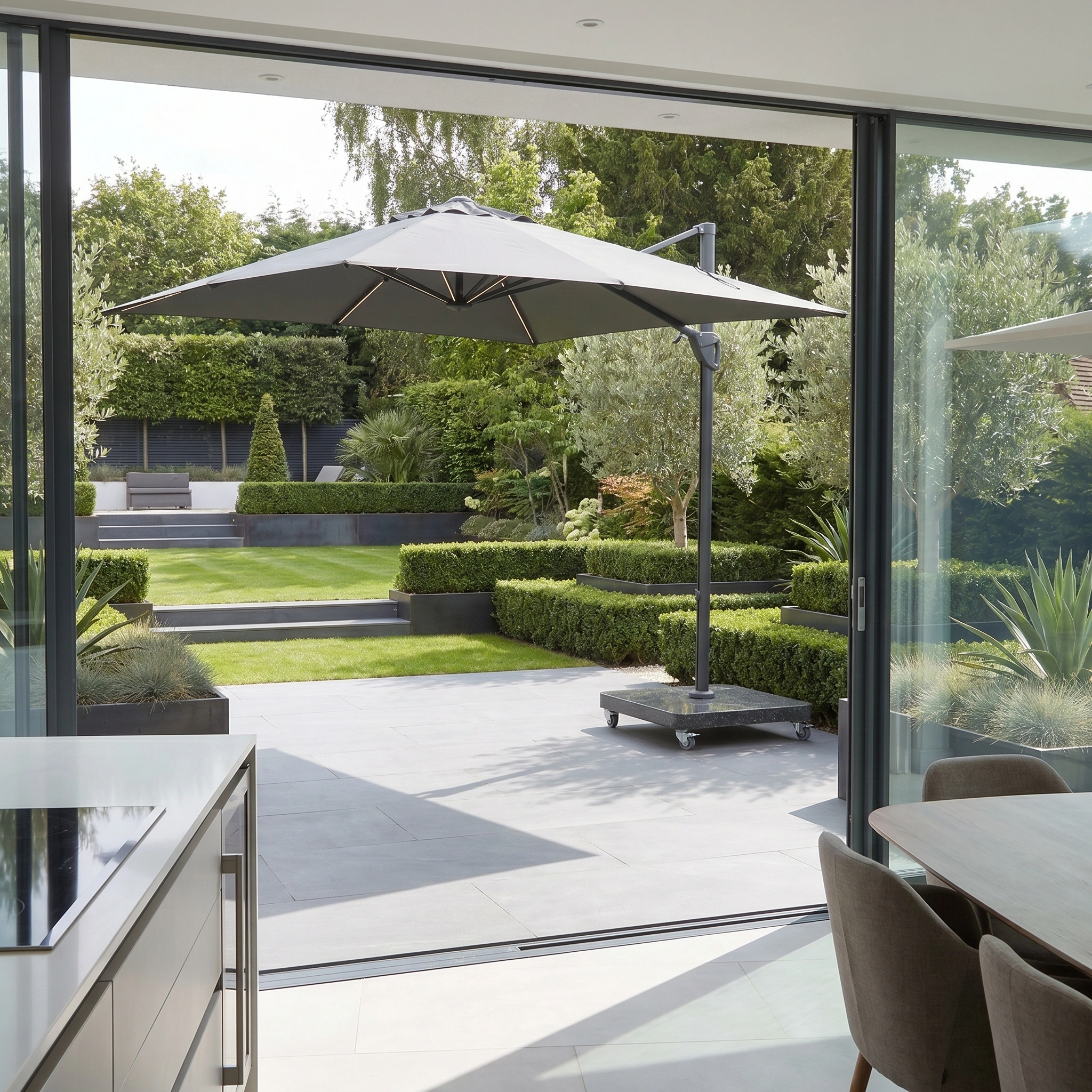 Modern patio featuring the Glow Challenger T2 3m Square Cantilever Parasol in Anthracite, a neatly trimmed garden, and sliding glass doors opening to the backyard.