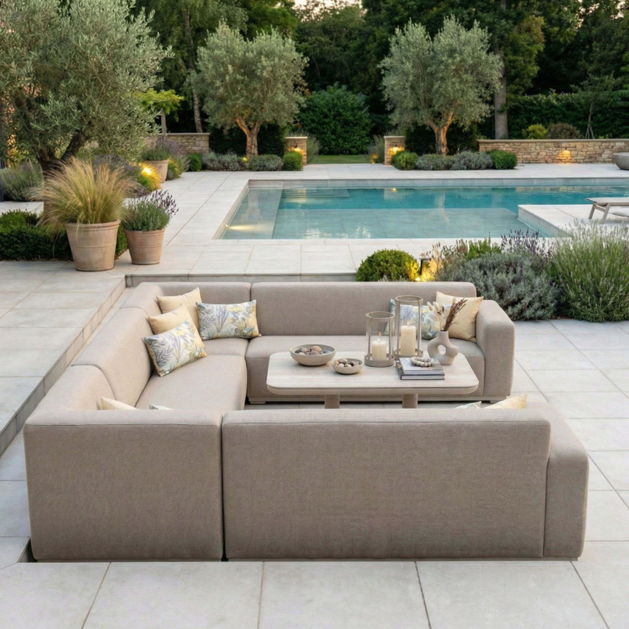 The Luna U-Shape Outdoor Fabric Sofa Set with Altura Rising Table in Fawn offers comfort and weather-resistant style, featuring plush pillows—ideal for relaxing by the pool, surrounded by greenery and potted plants.