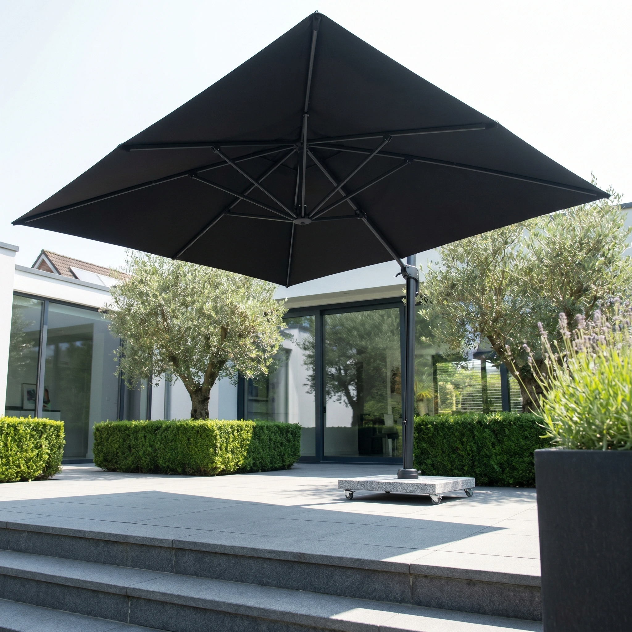The Glow Challenger T2 3m Square Cantilever Parasol in Anthracite stands on a modern outdoor terrace, with greenery and glass doors in the background.
