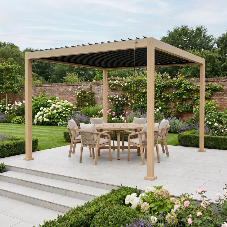 PergoSTET Lite Neo 3m x 3m Metal Square Pergola in Wood Effect, with tilting steel louvres, plus a round table and six chairs, set in a landscaped garden filled with flowers and greenery.