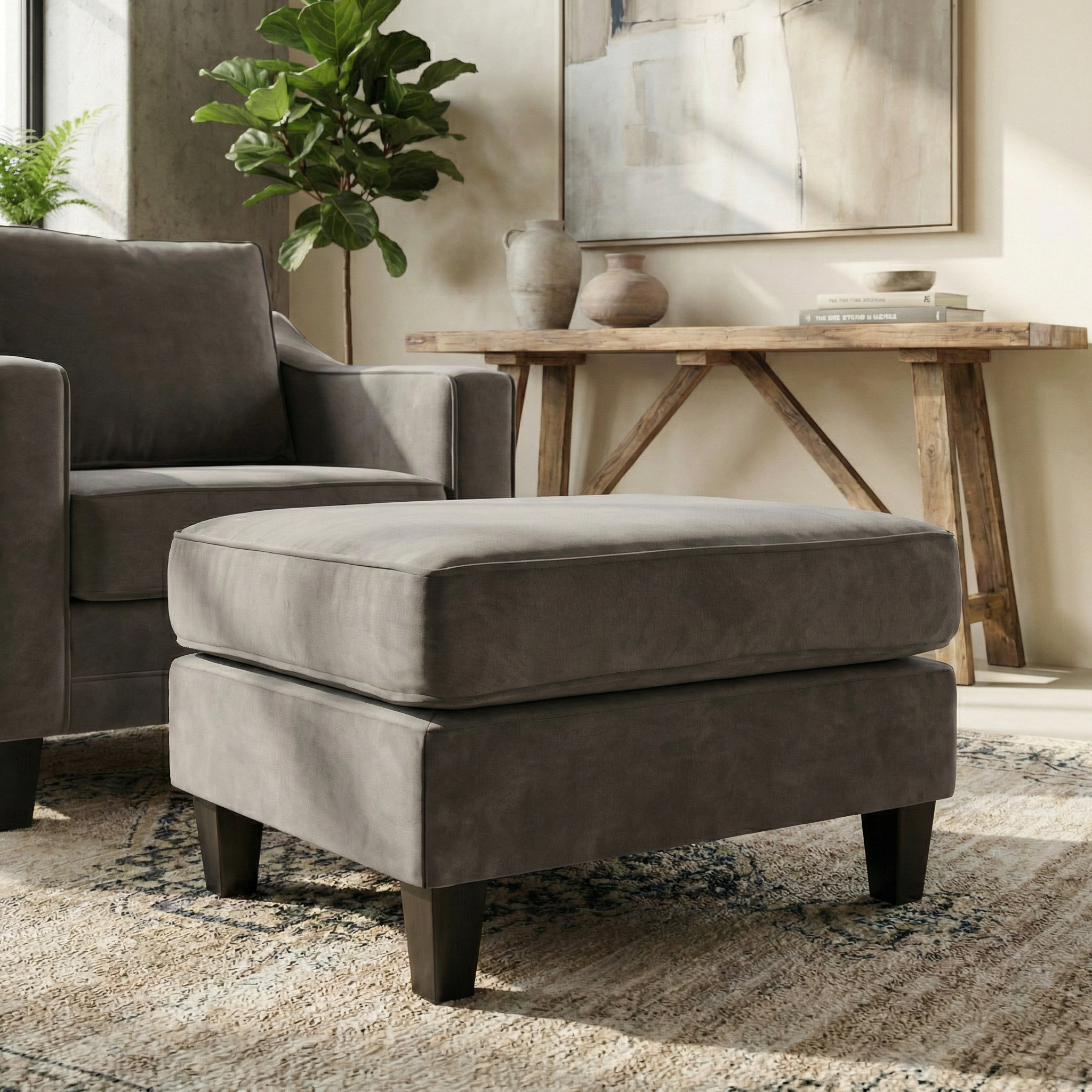 Gray upholstered armchair with a Wiltshire Velvet Footstool in Steel Grey in a cozy, sunlit living room, surrounded by lush plants and rustic decor.
