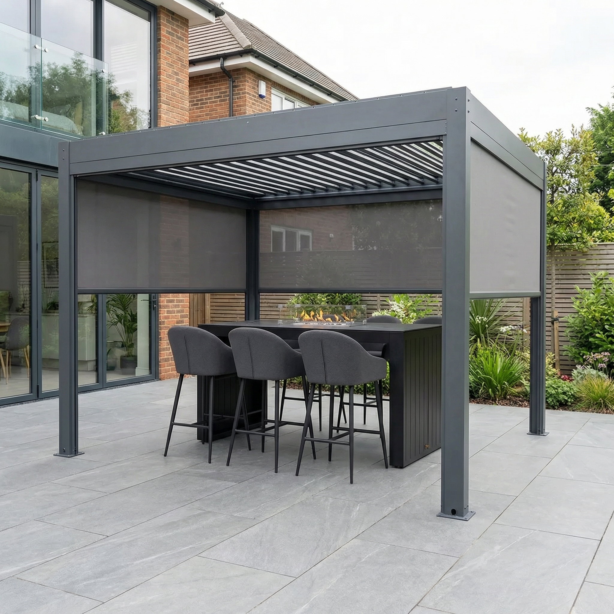 The PergoSTET Plus 3m x 3m Square Pergola in Grey, with LED lighting and 3 manual side blinds, adds style and comfort to your garden patio, featuring a bar table and four chairs beside your home.