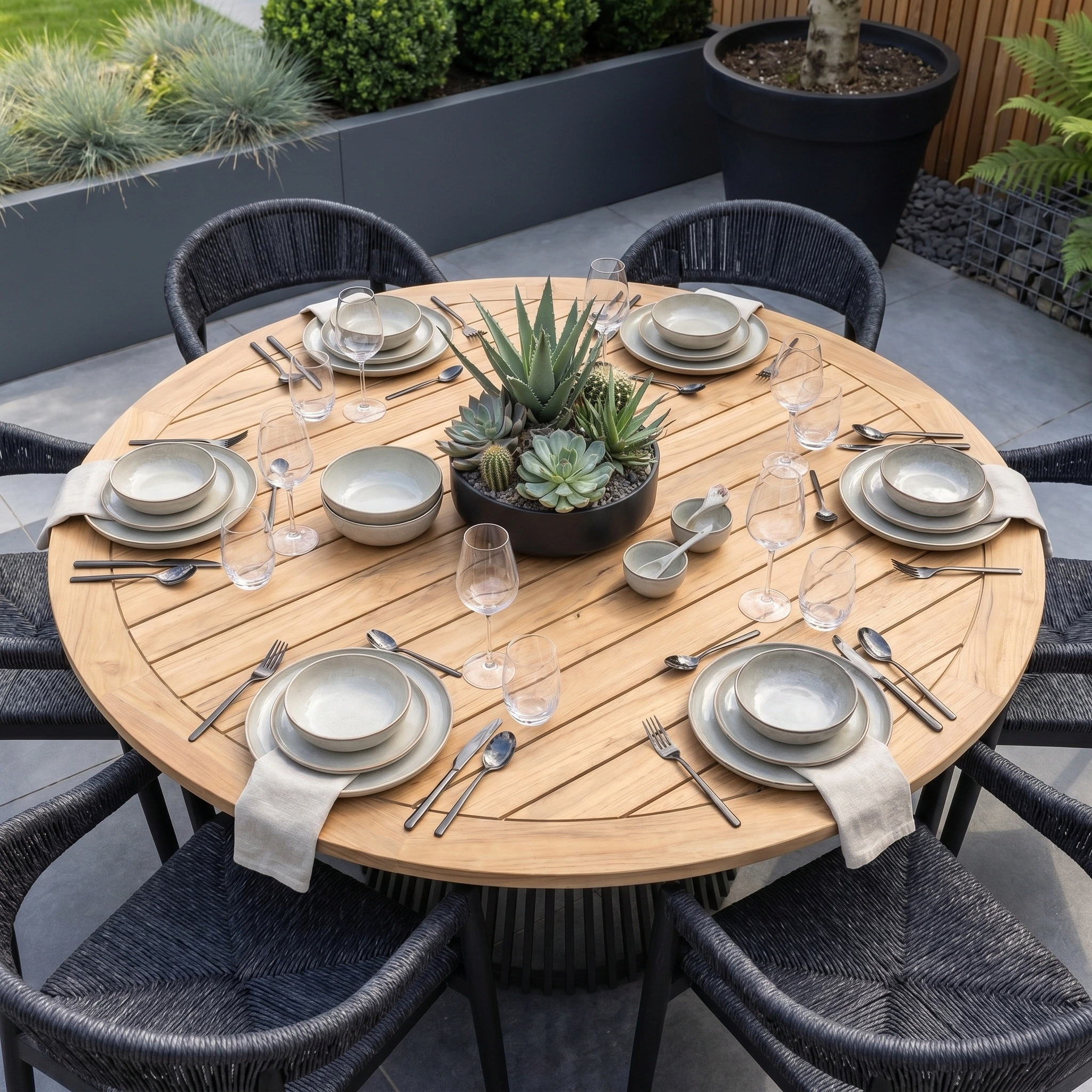 The Lucca 6 Seat Dining Set with Teak Round Table in Black is set for six with neutral dishware and a succulent centerpiece, highlighting elegant outdoor dining style.
