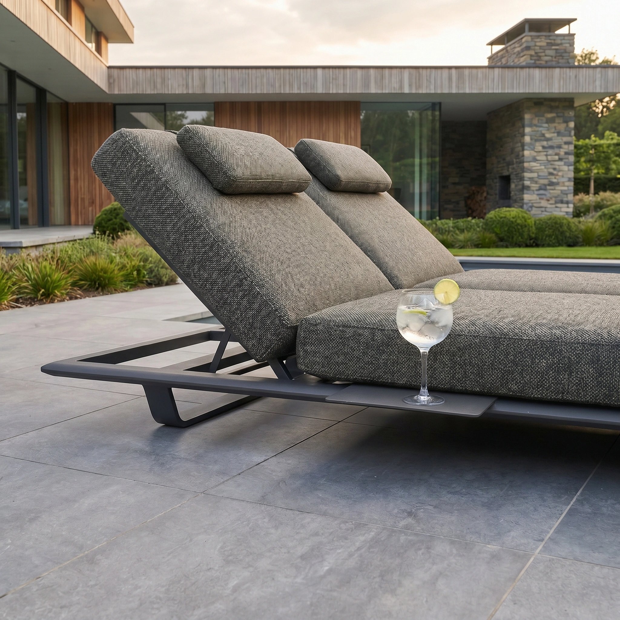The Hatia Double Sun Lounger with Side Table in Charcoal offers UV-resistant comfort for relaxing in style on your patio, complete with cushions and a convenient cocktail rest near your contemporary home.