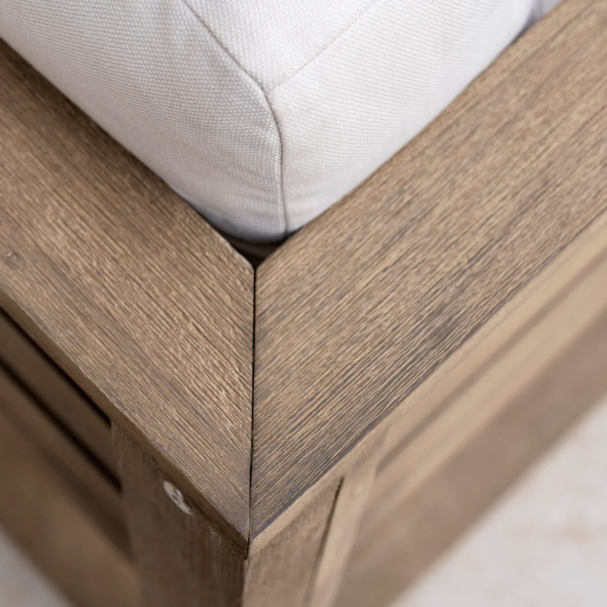 Close-up of a weathered brown wood corner frame with a beige cushion from the Andora Corner Sofa Set with Coffee Table/Footstool—perfect for pairing with your favorite outdoor or modular garden furniture.