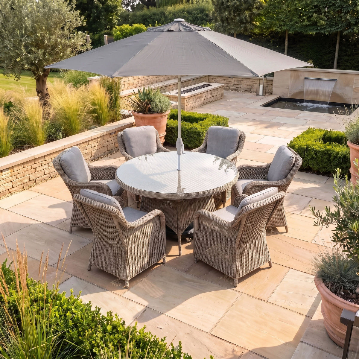Create an inviting backyard oasis with the Isla 6 Seat Round Dining Set in Flint, featuring six elegant wicker chairs and a gray umbrella—the ideal outdoor dining furniture for gatherings in any landscaped garden.