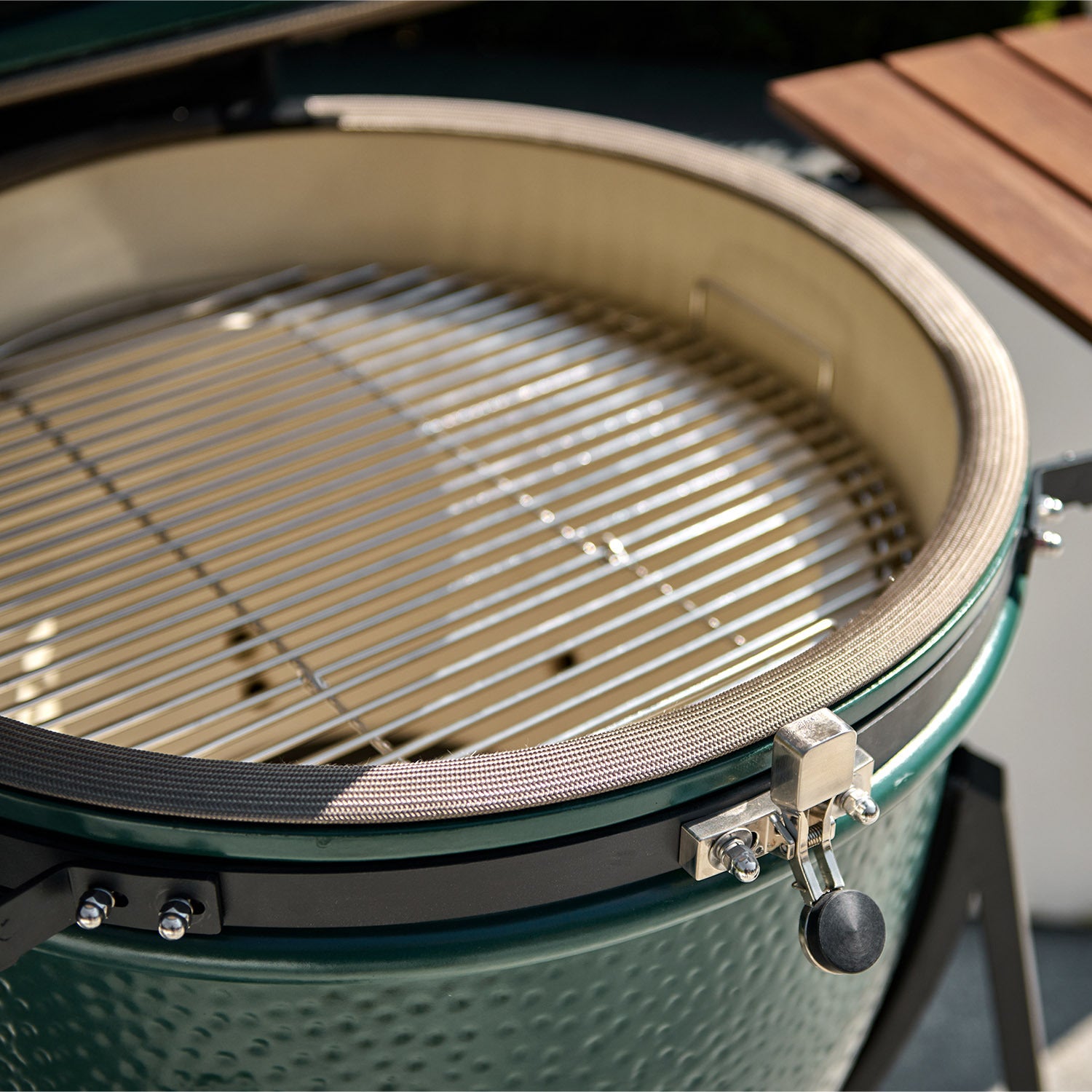 Close-up of an open Kamado BBQ 22" Ceramic Grill in Matte Green with stainless steel grates and a wooden side shelf.